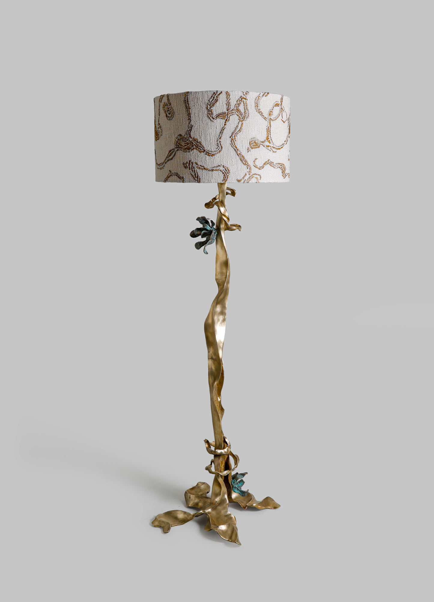 Decorative floor lamp with a sculptural brass base resembling twisting branches and leaves, topped with a fabric lampshade featuring a botanical embroidery pattern in neutral tones.