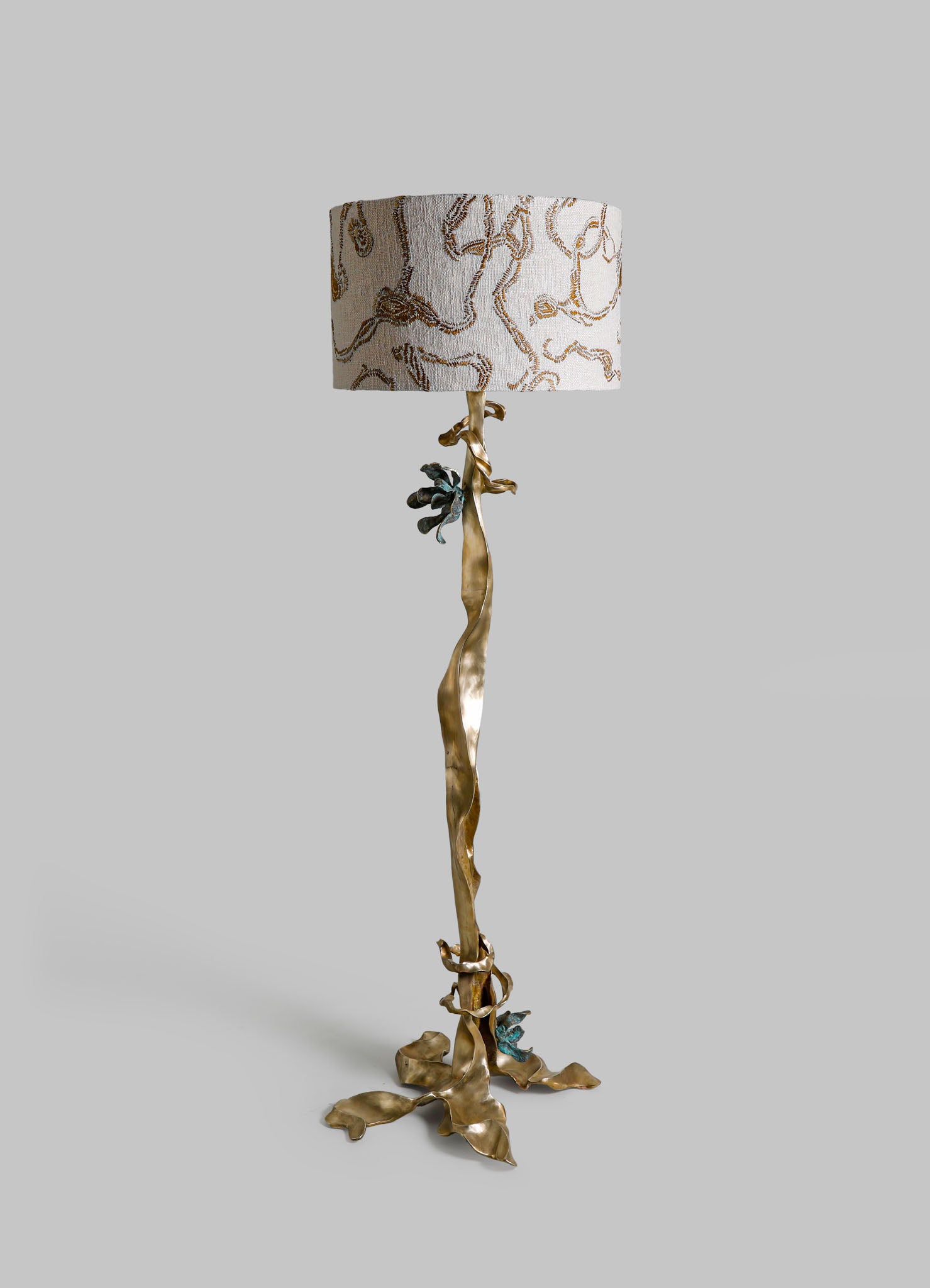 Decorative floor lamp with a sculptural brass base resembling twisting branches and leaves, topped with a fabric lampshade featuring a botanical embroidery pattern in neutral tones.