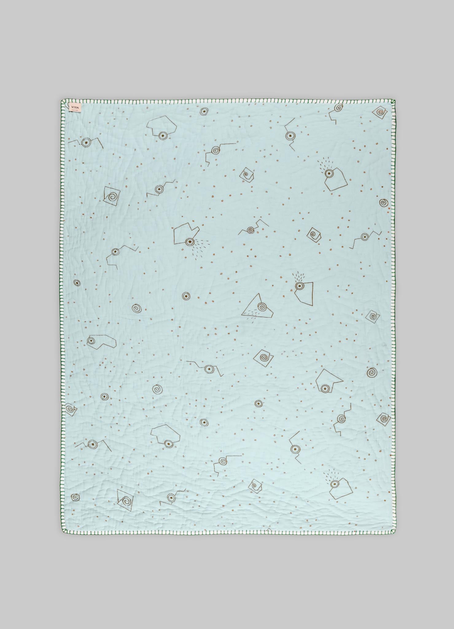 Quilt with a light pastel blue cotton fabric featuring geometric and abstract motifs in brown and black, finished with a striped edge border.