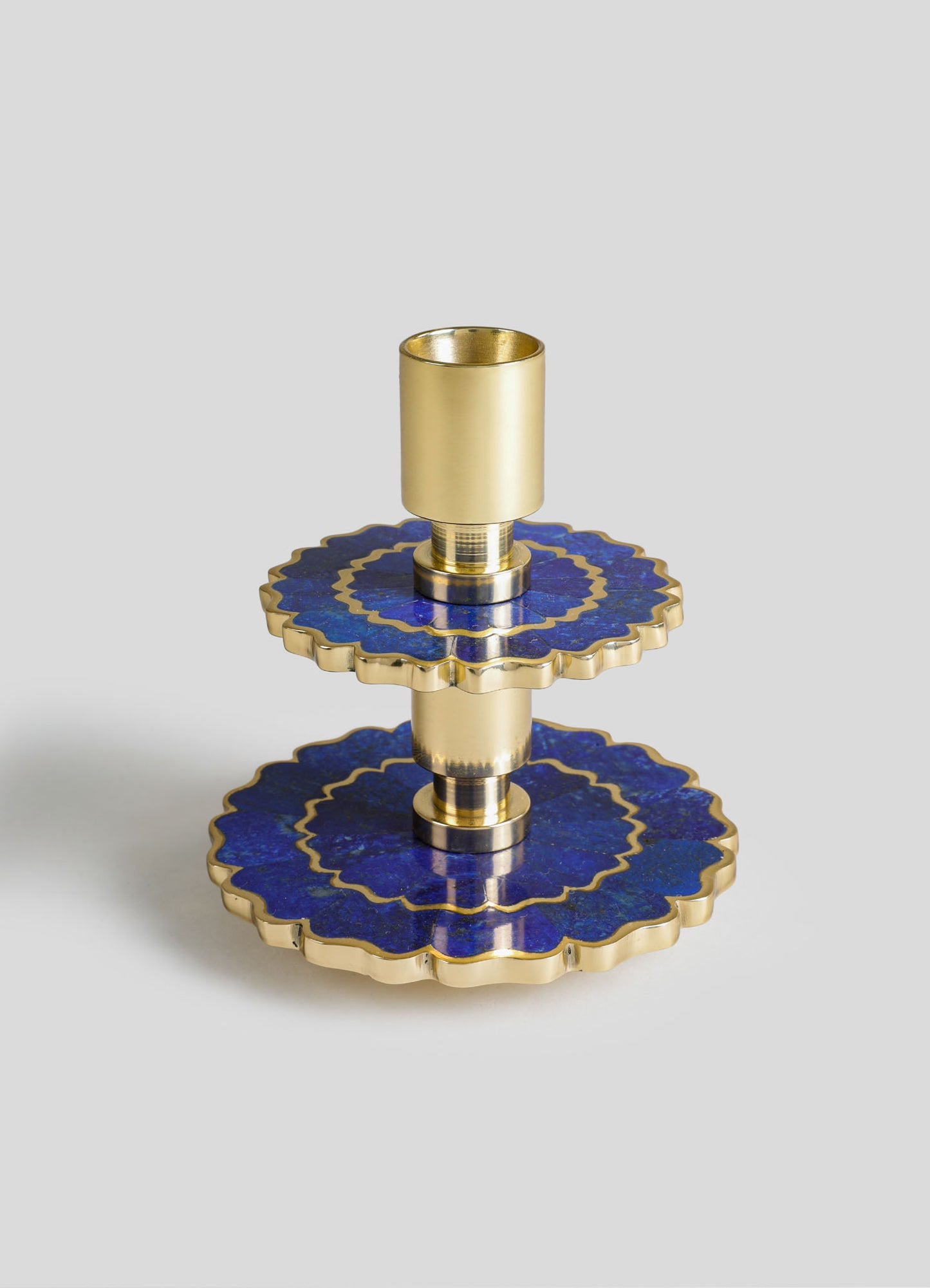 Brass candlestick holder with a tiered design and circular, scalloped blue and gold inlays, featuring a cylindrical cup for holding candles.