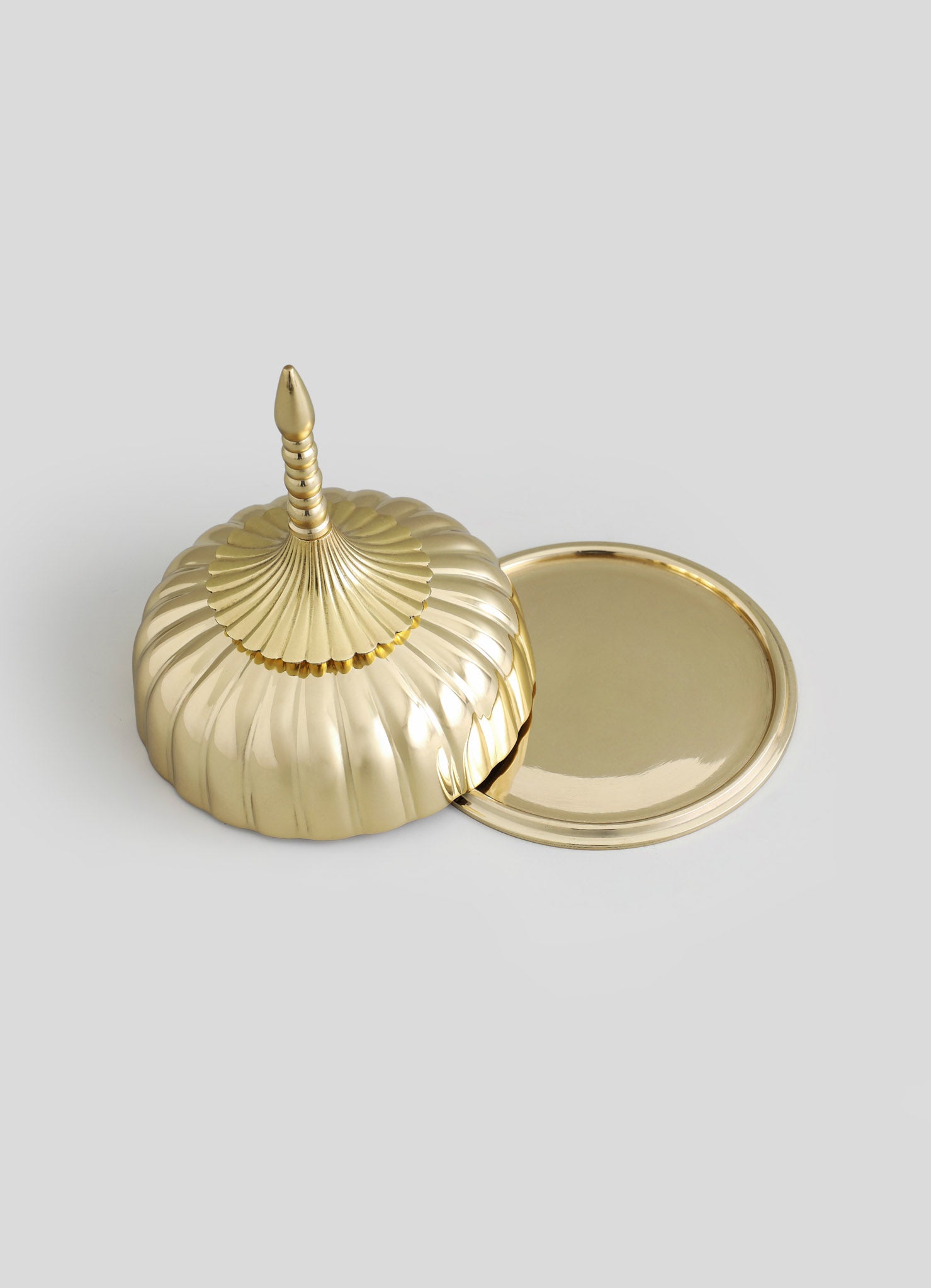 A gold-colored decorative box with a scalloped, ridged surface and a pointed finial on the lid, accompanied by a matching round tray. The set features a shiny metallic finish and elegant, vintage-inspired design.