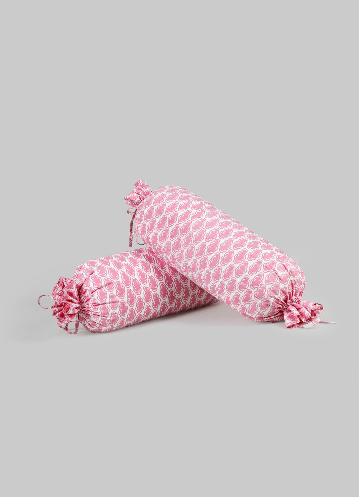 Pink fabric bolster cushions with a floral pattern, closed with fabric ties and gathered ends, made from soft textile material.