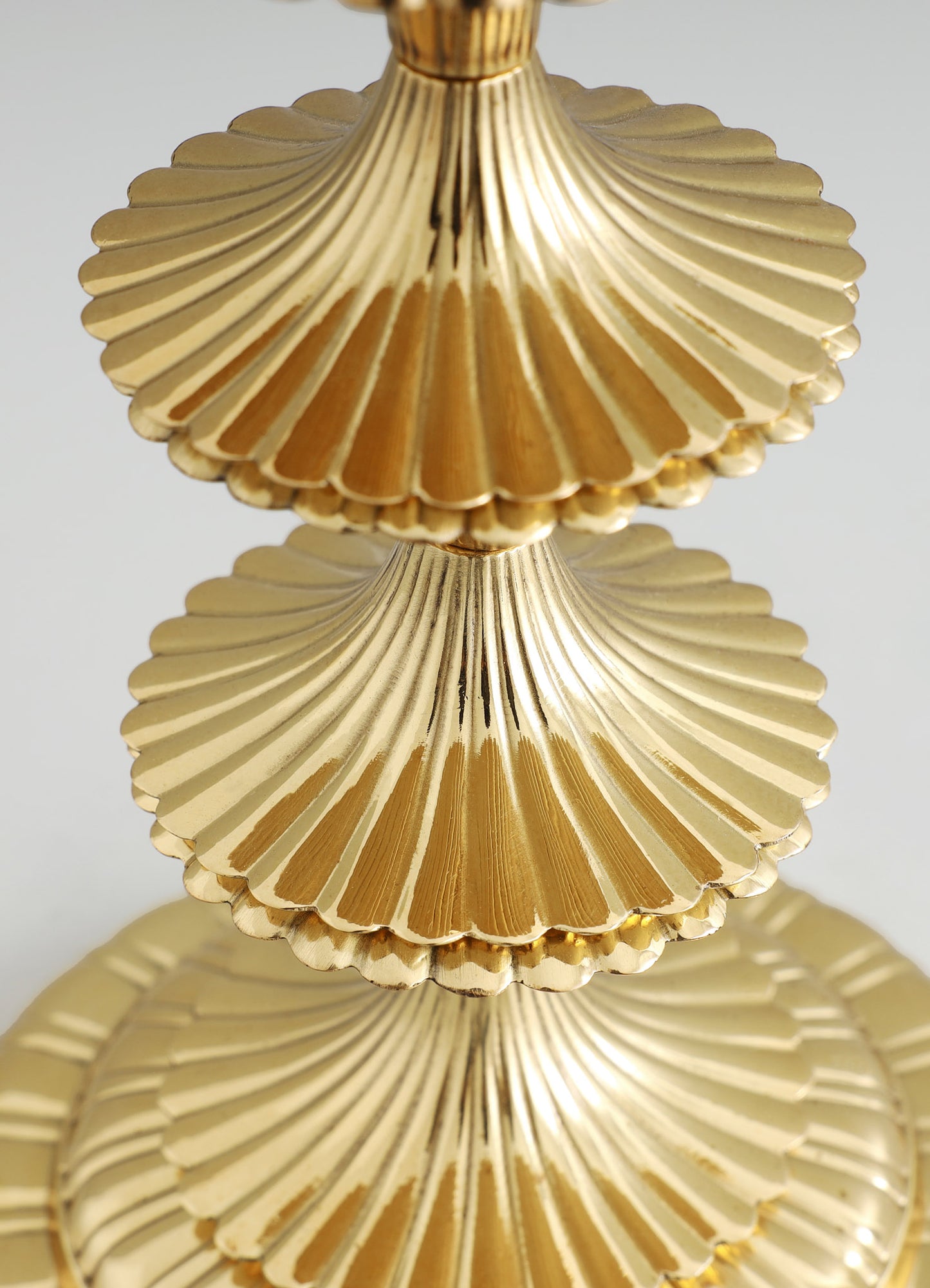 Gold-colored decorative tiered stand with scalloped edges and a ribbed texture, made of metal with a shiny finish, arranged in a vertical stack.