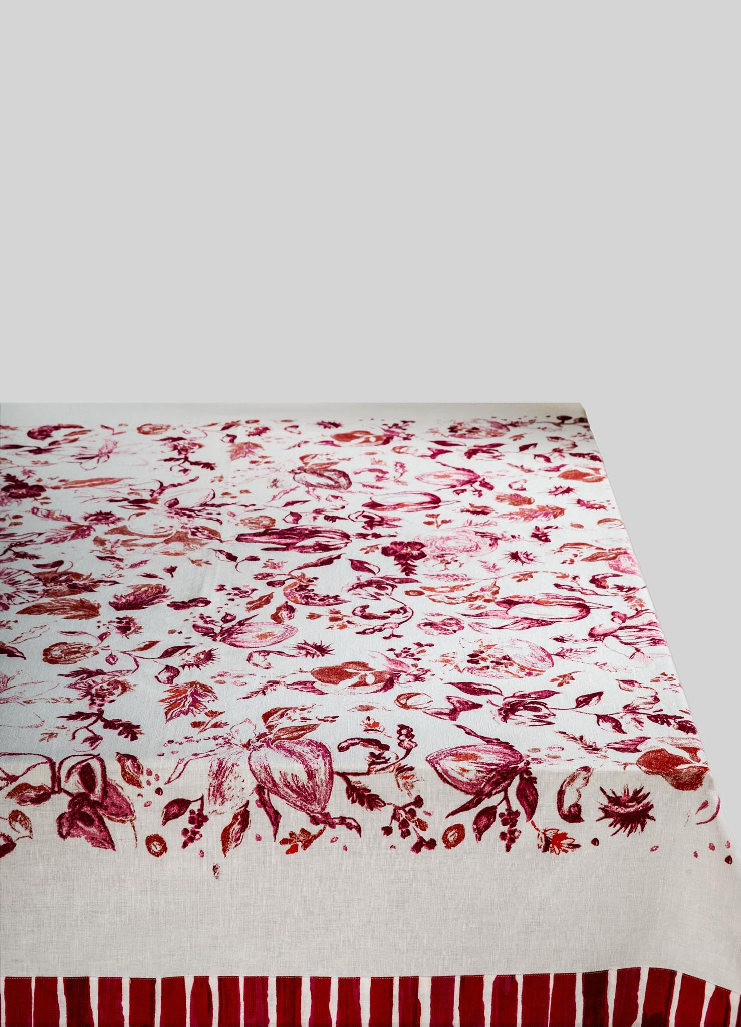 A tablecloth with a floral print pattern in shades of red and pink on a white background, featuring botanical motifs and a striped border at the edge.