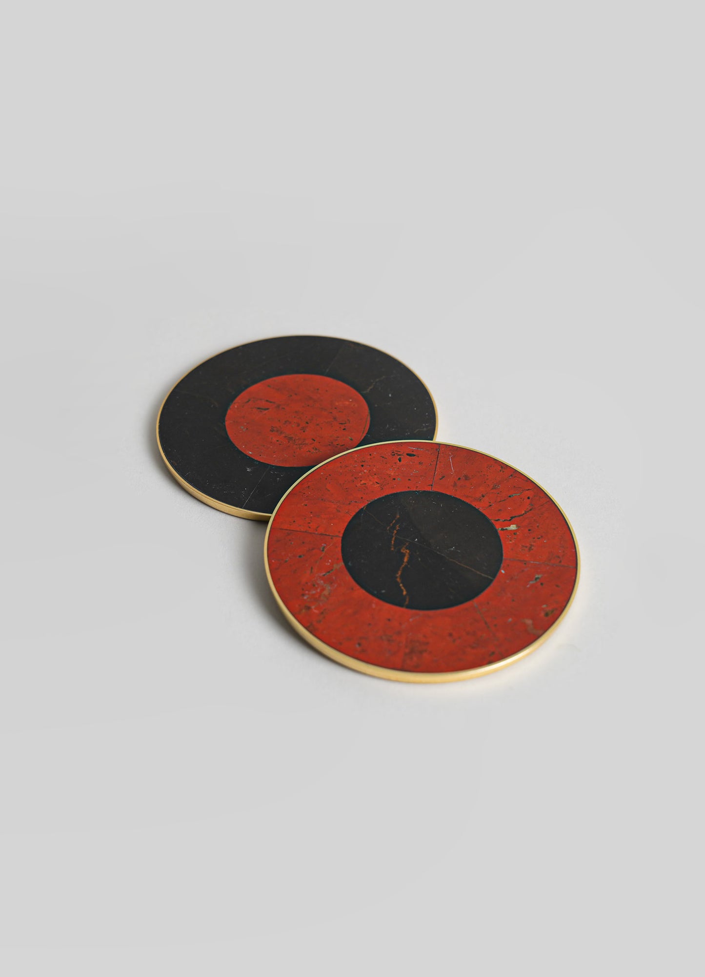 Circular marble coasters with red and black color blocks and gold trim, featuring a smooth, polished surface.
