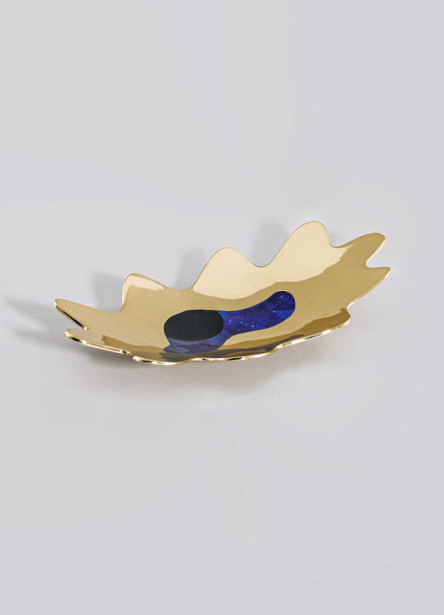 A decorative ceramic bowl with an organic, leaf-like shape, glazed in a glossy gold finish with a navy and black abstract motif inside. The design combines modern elegance with handcrafted artisan style.