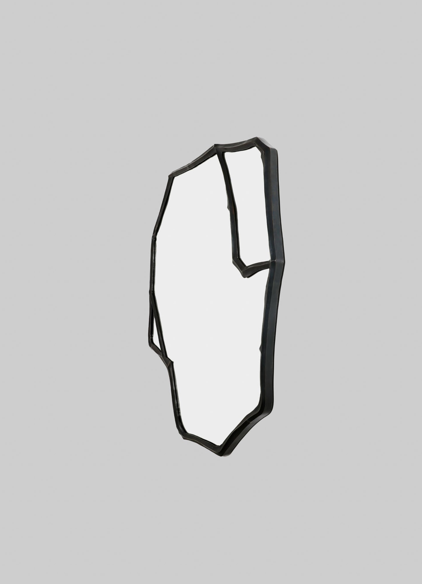 A black metal wall mirror with an irregular, geometric frame design, set against a plain light gray background.
