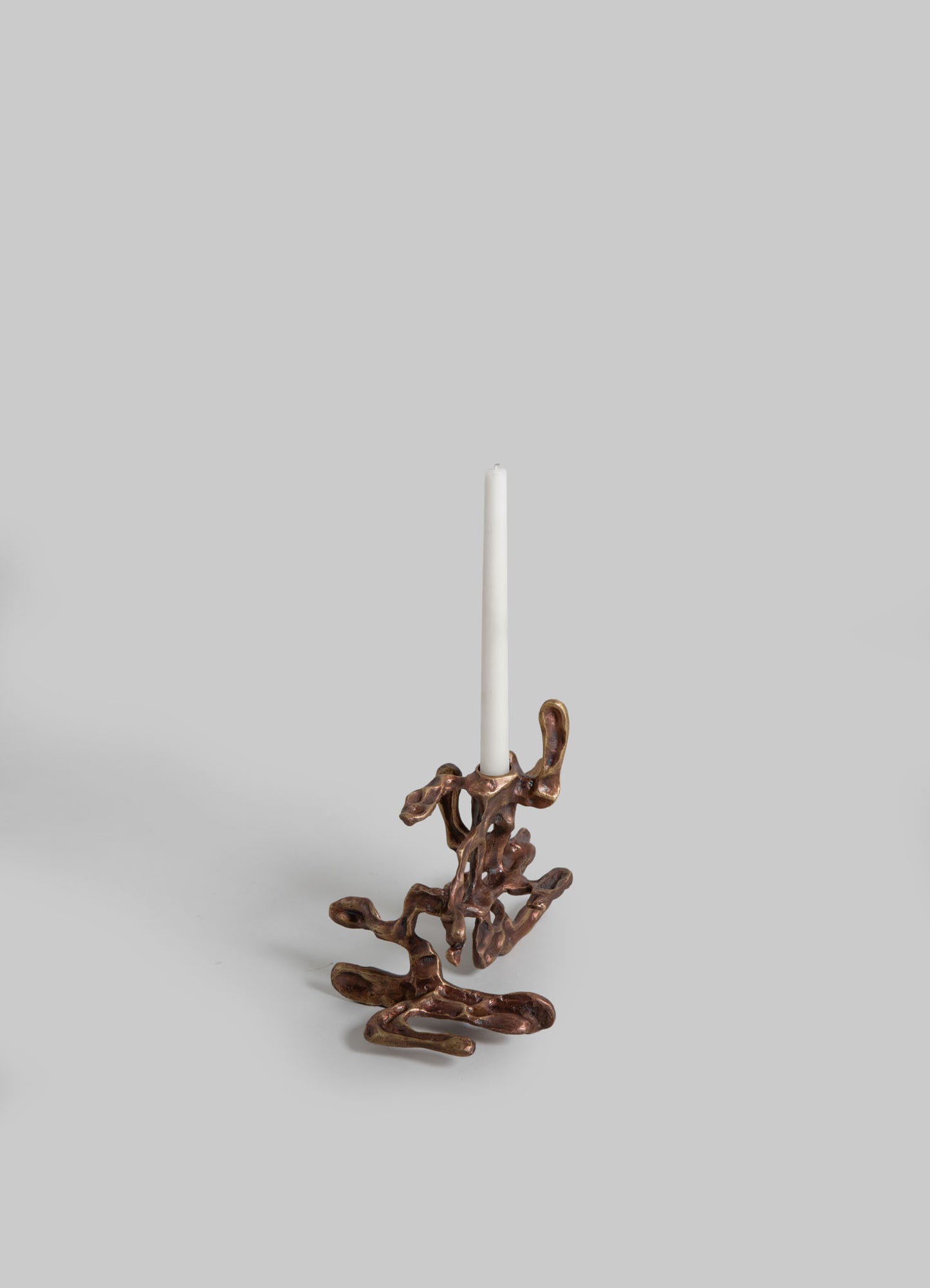 A sculptural brass candle holder with an organic, abstract form and a polished metallic finish, holding a white taper candle.