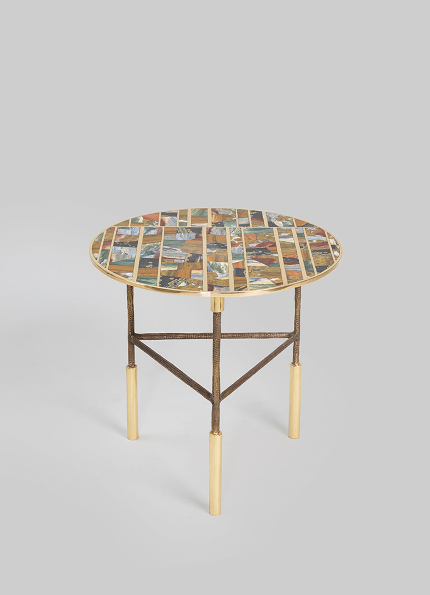 A round side table with a mosaic tile top featuring geometric patterns in earthy tones and small patches of blue, supported by a metal frame with gold-colored legs.