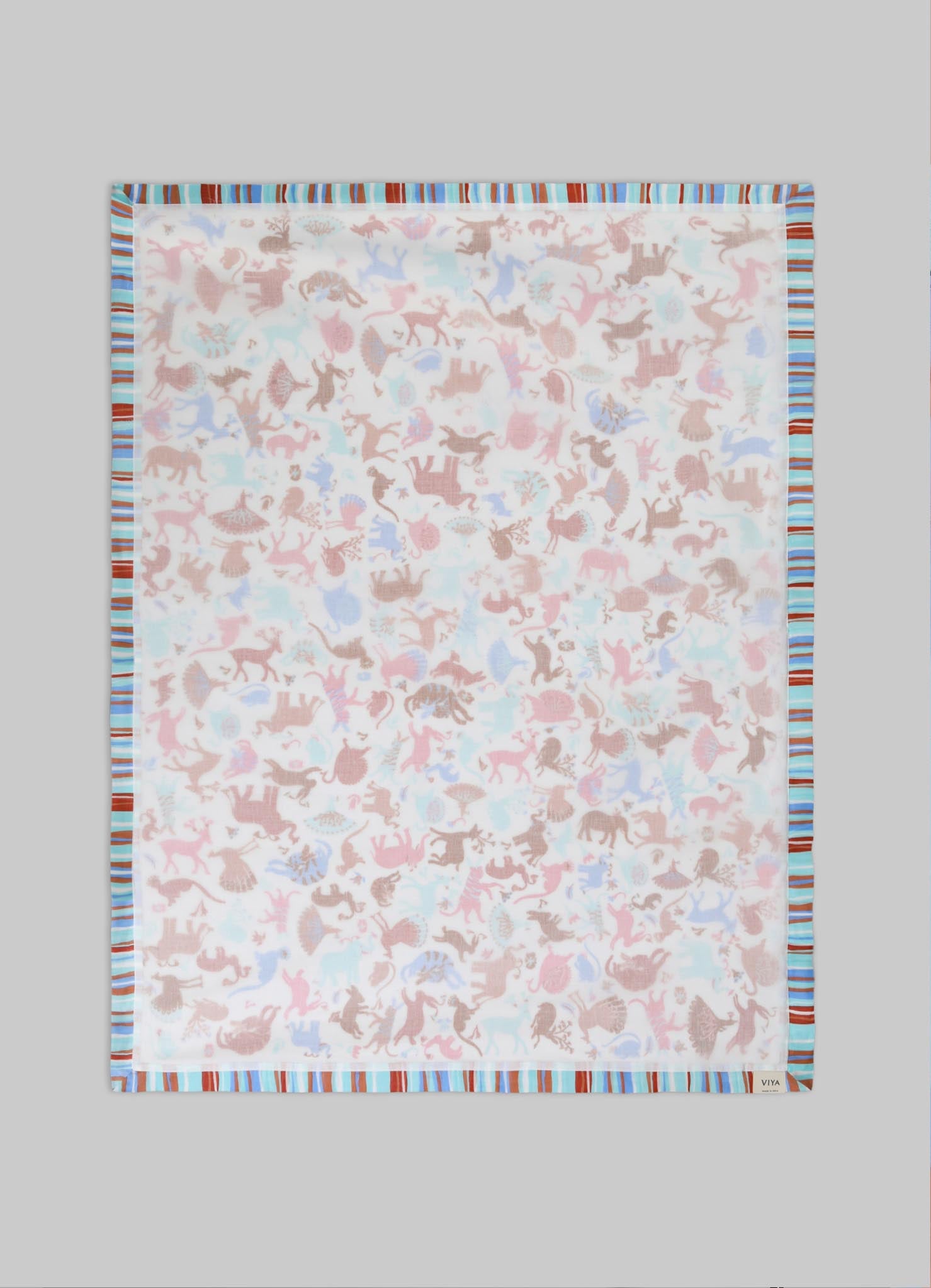 A lightweight cotton or linen scarf with a pastel-colored animal motif print in shades of pink, blue, and beige, bordered by multicolored stripes in red, blue, and white, on a neutral background.