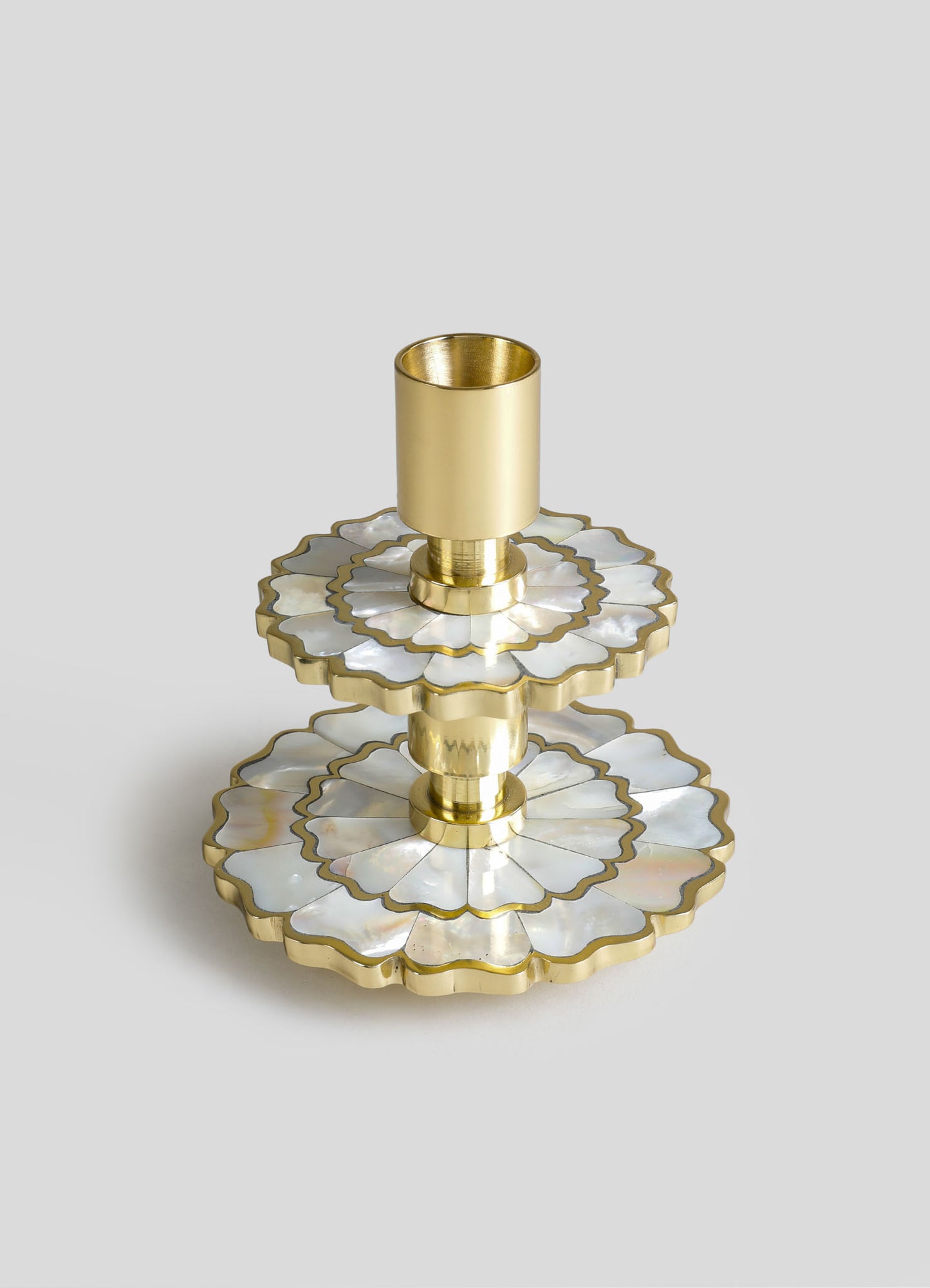 A decorative brass candle holder with layered mother-of-pearl inlay, featuring scalloped edges and a polished gold finish, arranged on a light gray background.