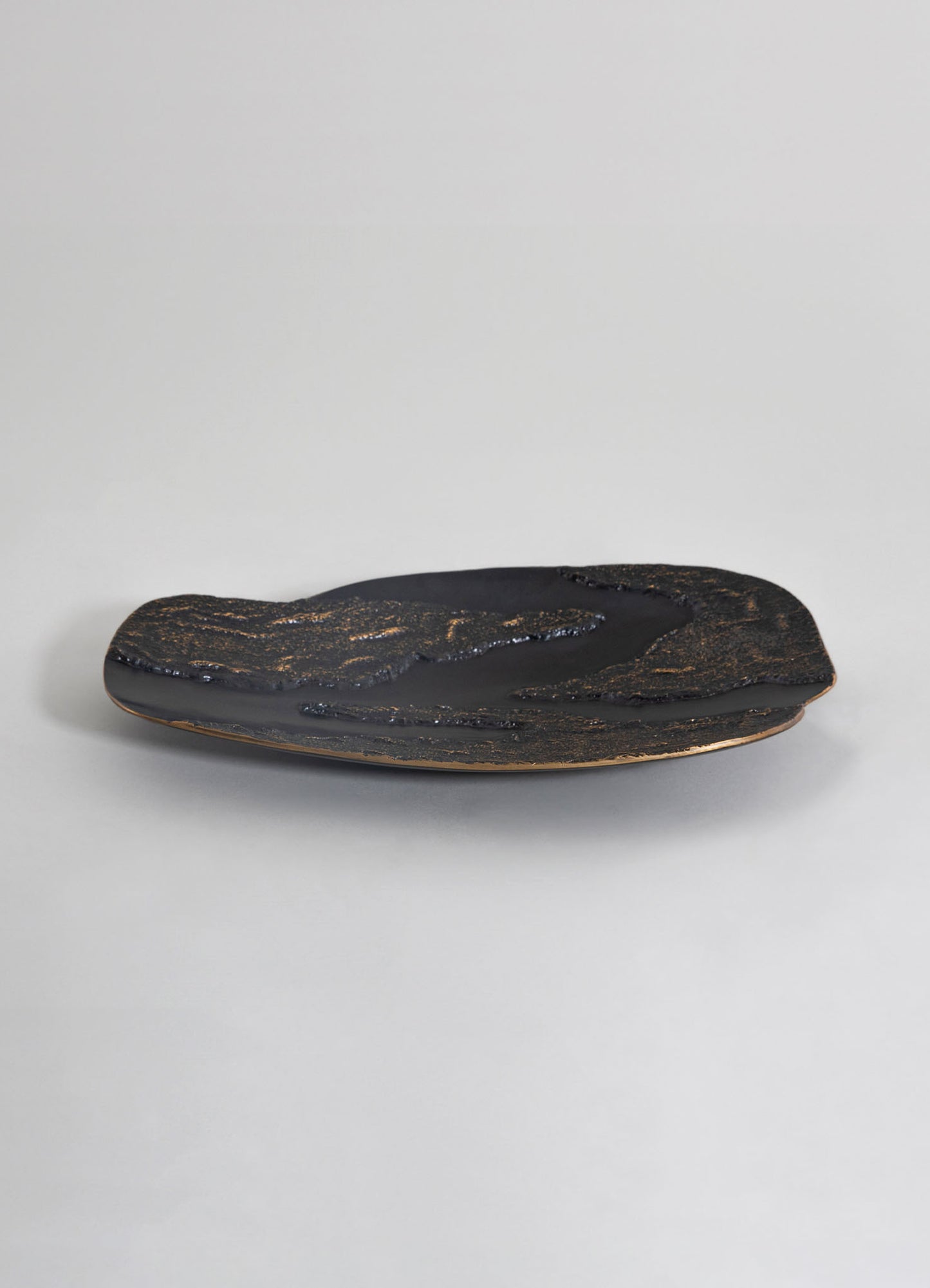 A black ceramic tray with an irregular, organic shape and textured surface featuring gold accent details, set against a plain light background.