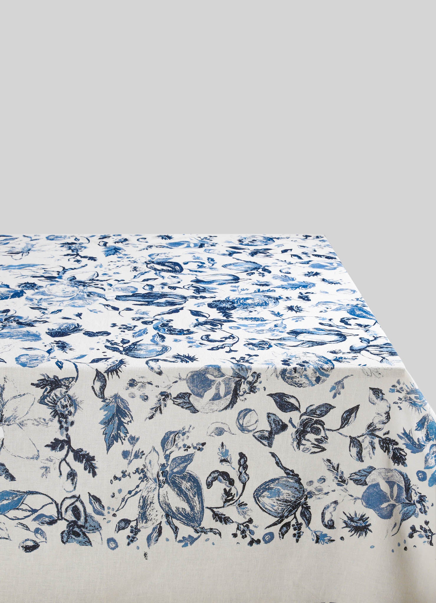 Cotton tablecloth with a blue and white floral pattern featuring detailed botanical motifs and foliage, set against a plain background.
