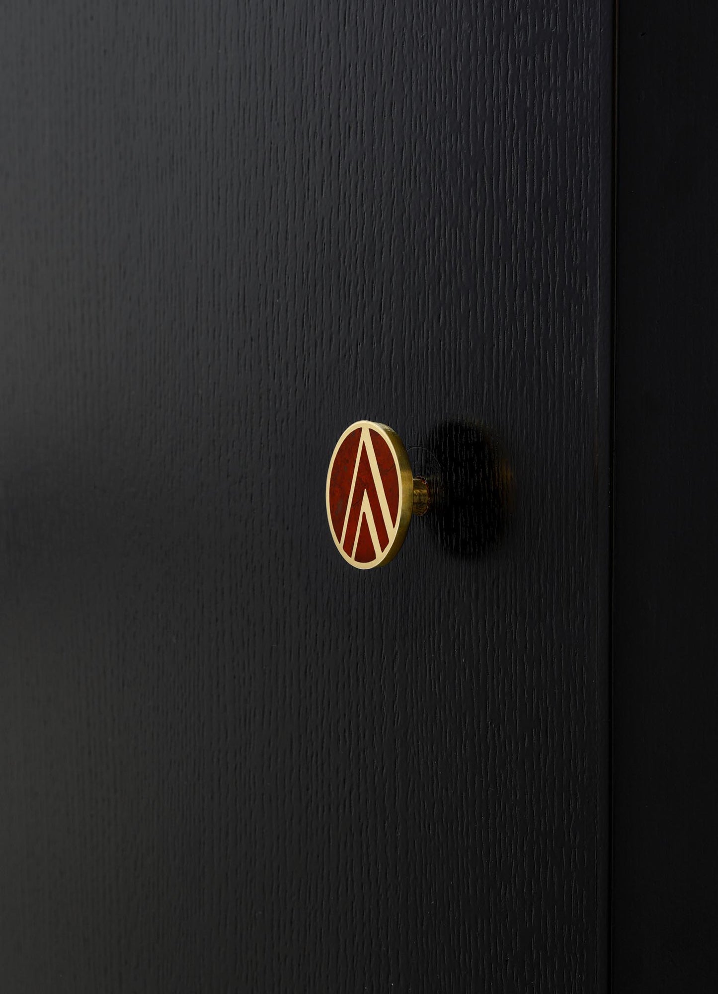 A black wooden door with a textured surface and a round, decorative doorknob featuring a gold edge and a red and white geometric motif.