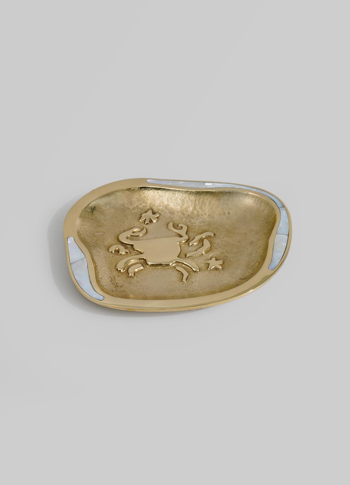 A decorative brass dish with a crab motif embossed in the center, featuring a smooth, rounded shape and polished finish. The dish has white inlays on the rim and a textured interior surface.