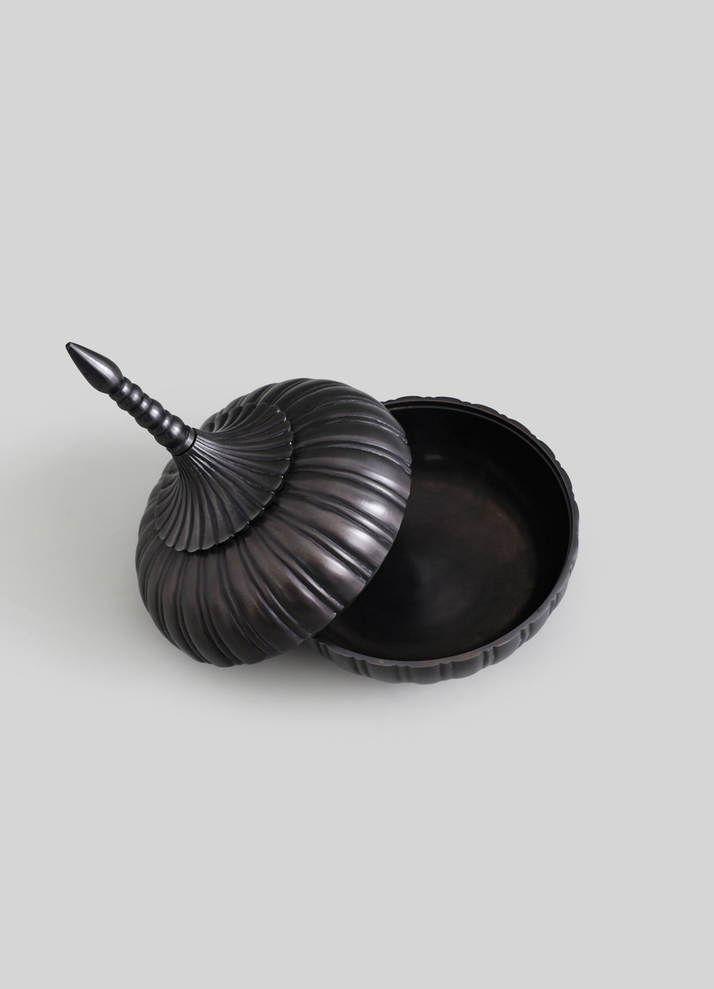 Black decorative bowl with a matching lid and finial, featuring a ribbed, shell-like texture and a matte finish.