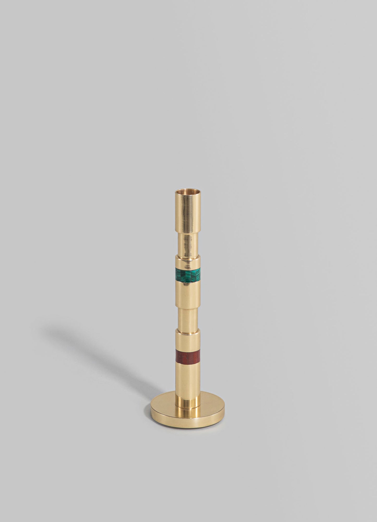 A brass candlestick holder with a cylindrical shape and a layered design featuring green and red accents, standing on a flat surface against a plain background.