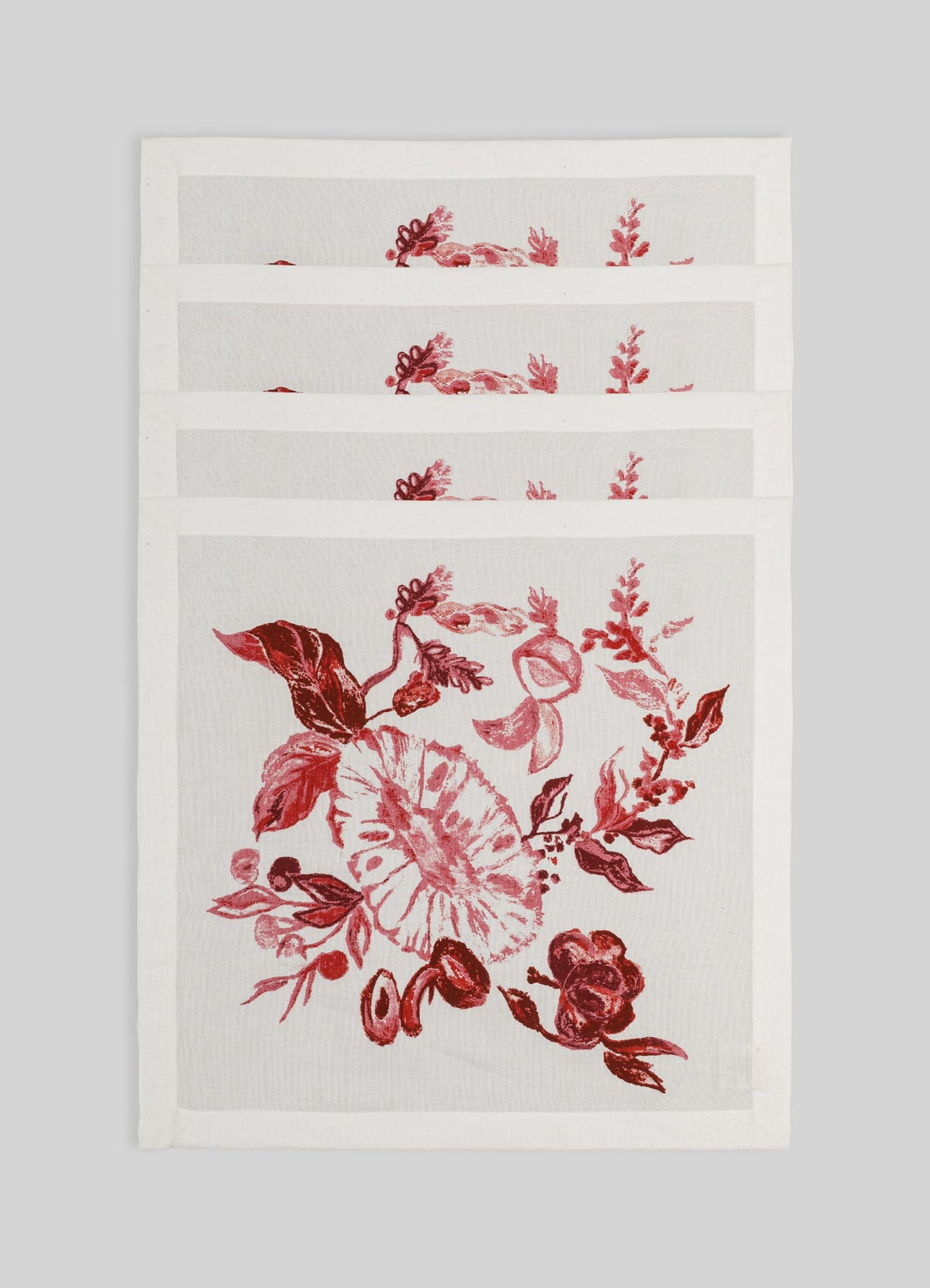 Cotton placemats with a floral print in shades of red and pink on a white background, featuring a botanical motif with leaves and flowers, arranged in a row on a plain surface.