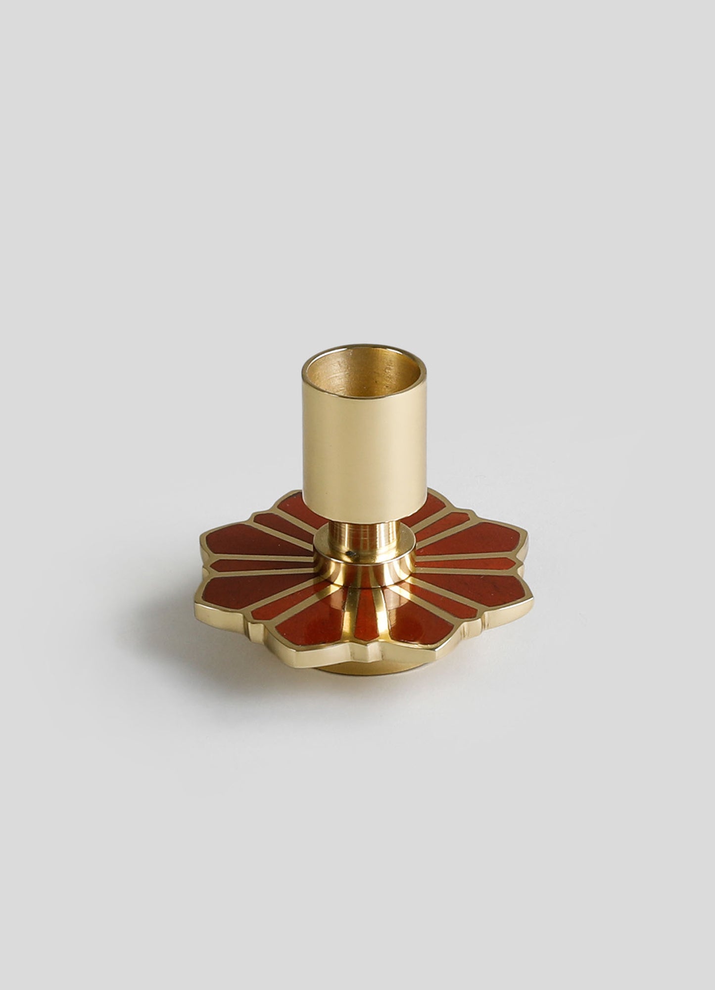 A brass candle holder with a cylindrical holder and a decorative base featuring a geometric pattern in reddish-brown and gold tones.
