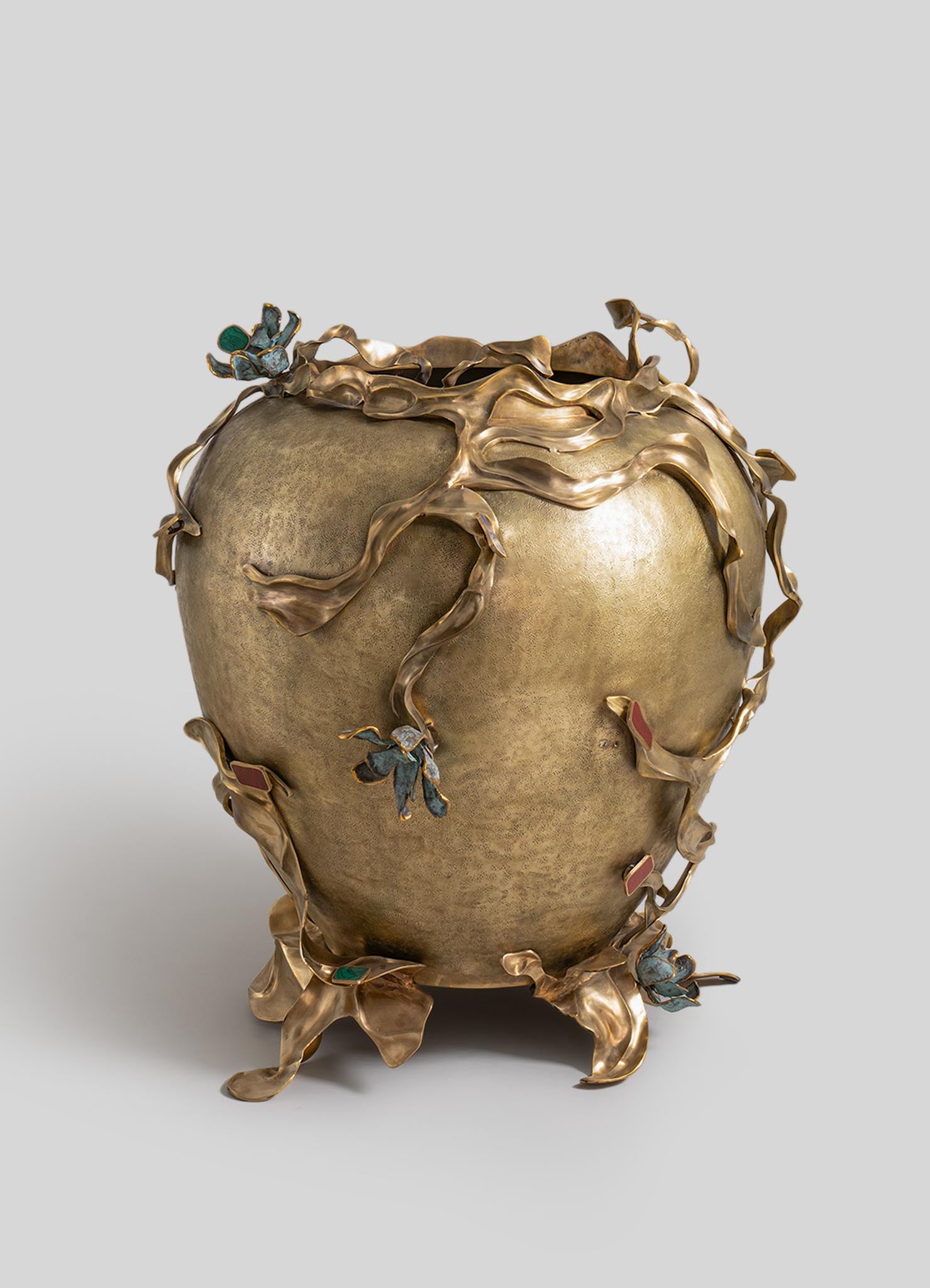 A decorative vase with a rounded body made of metal with a gold-tone finish, featuring intricate leaf and flower motifs with colorful enamel accents and a sculptural, organic design.