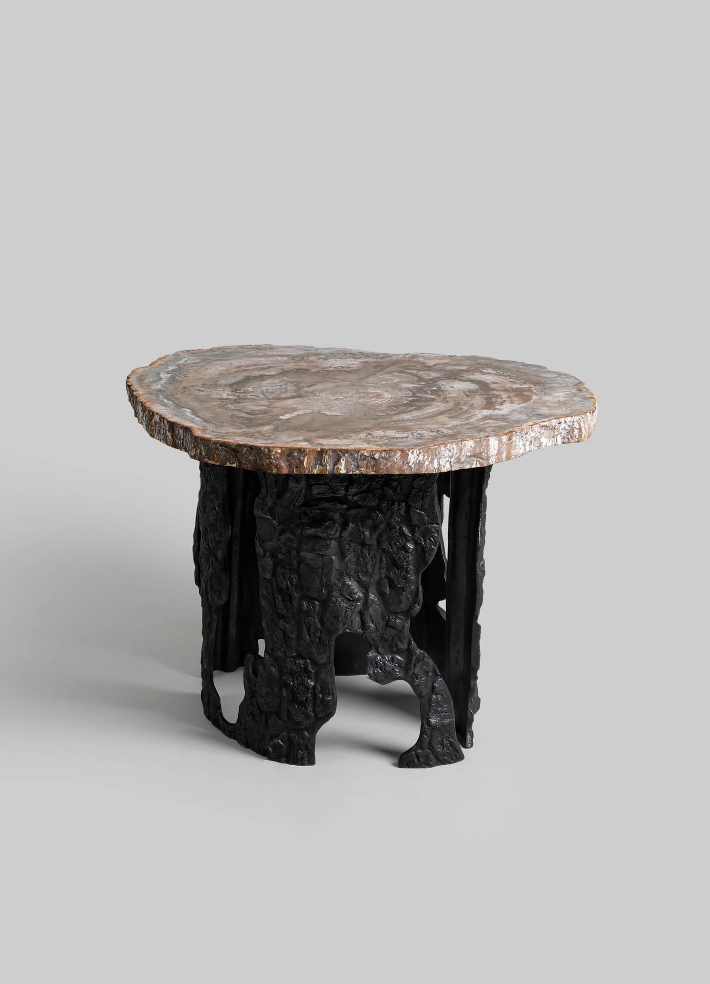 A small side table with a thick, rounded marble top featuring natural swirls and earthy tones, supported by a sculptural black metal base resembling tree roots or organic forms.