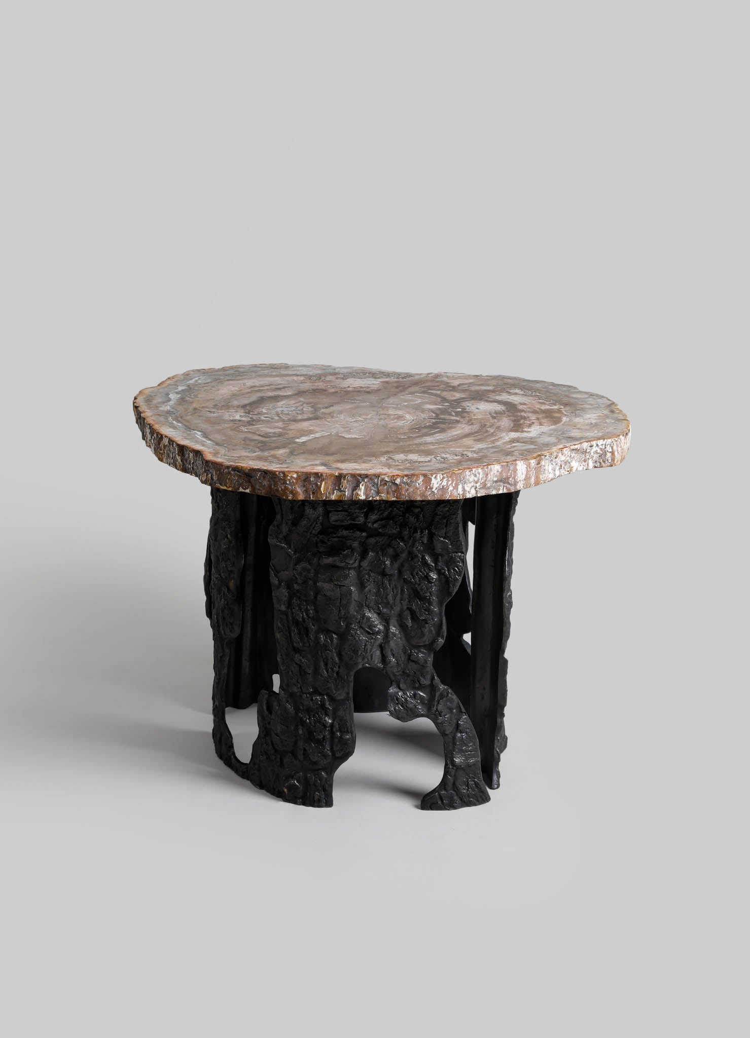 A small side table with a thick, rounded marble top featuring natural swirls and earthy tones, supported by a sculptural black metal base resembling tree roots or organic forms.