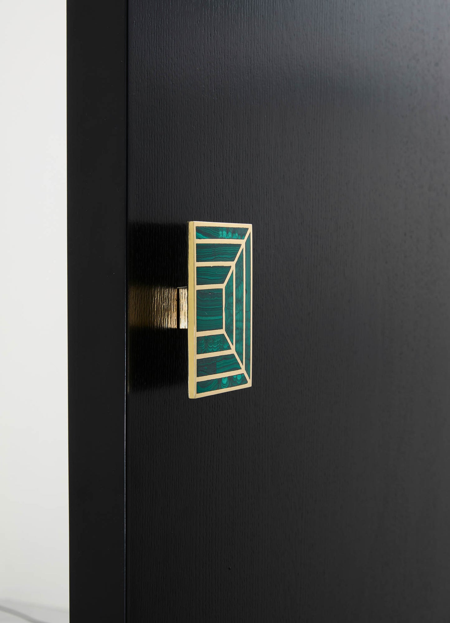 A decorative door handle features a geometric stained glass motif with shades of green and a wooden frame, mounted on a black door with a matte finish.