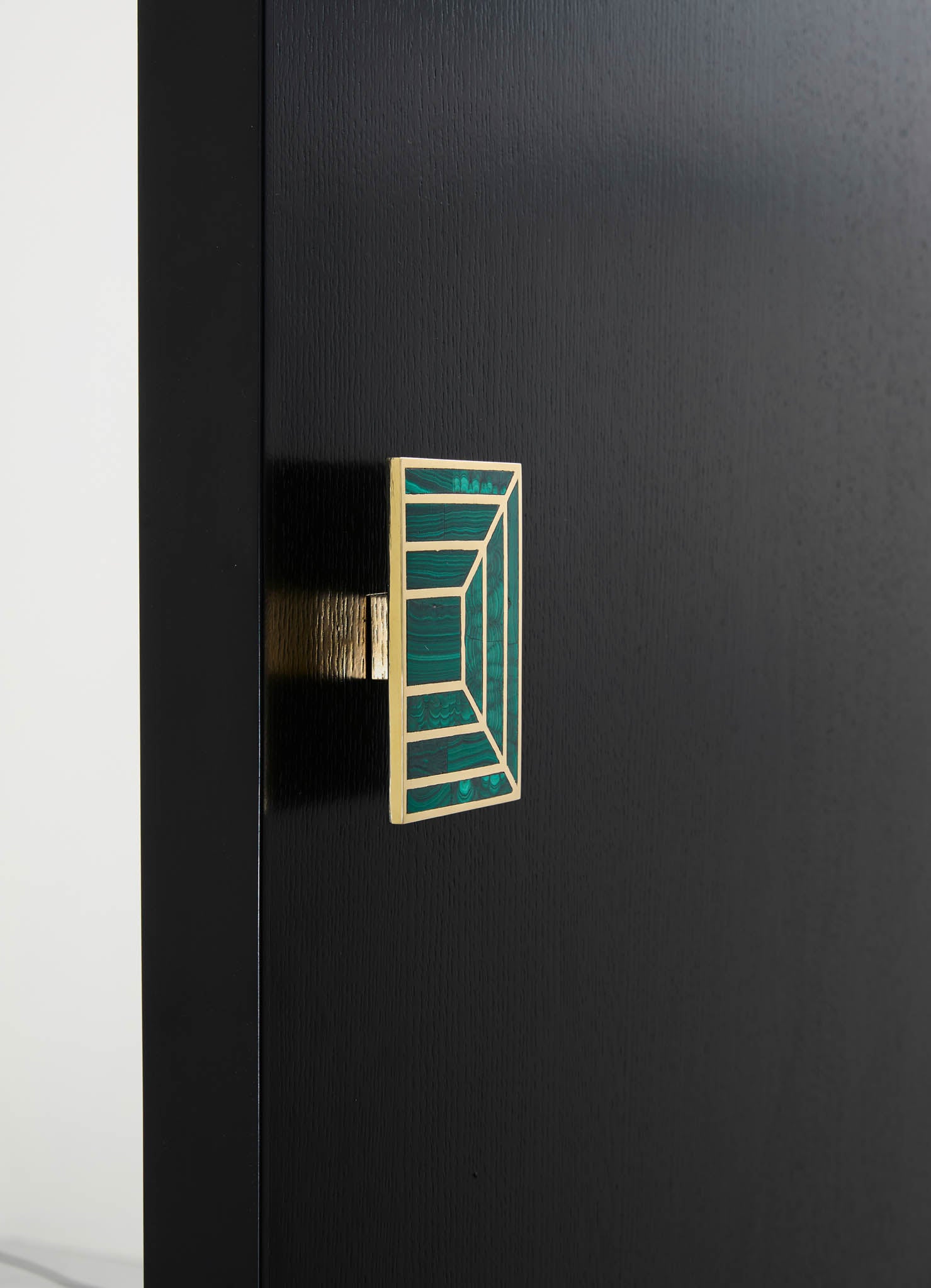 A decorative door handle features a geometric stained glass motif with shades of green and a wooden frame, mounted on a black door with a matte finish.