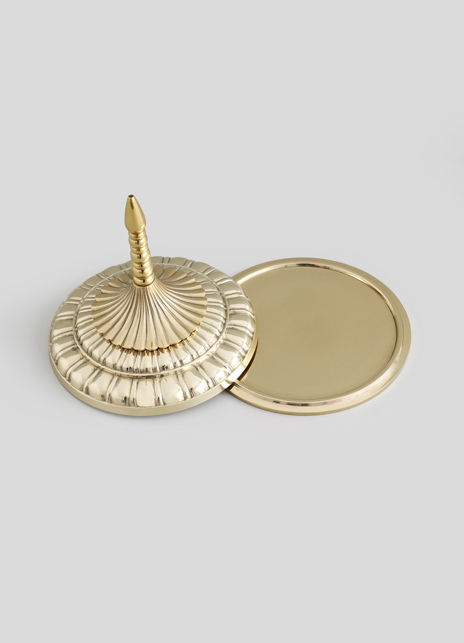A gold-toned brass tray with a domed, spiral-patterned lid featuring a pointed finial, and a matching round mirror with a smooth border.