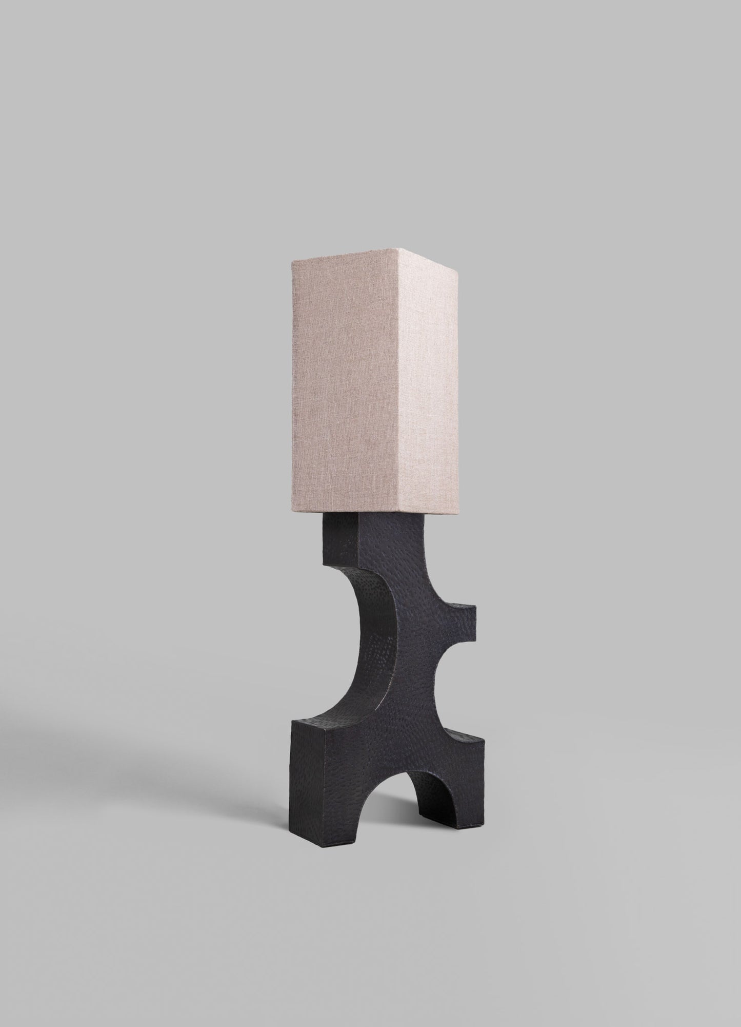 A modern table lamp featuring a black textured wood base with a distinctive curved design and a rectangular beige fabric lampshade.
