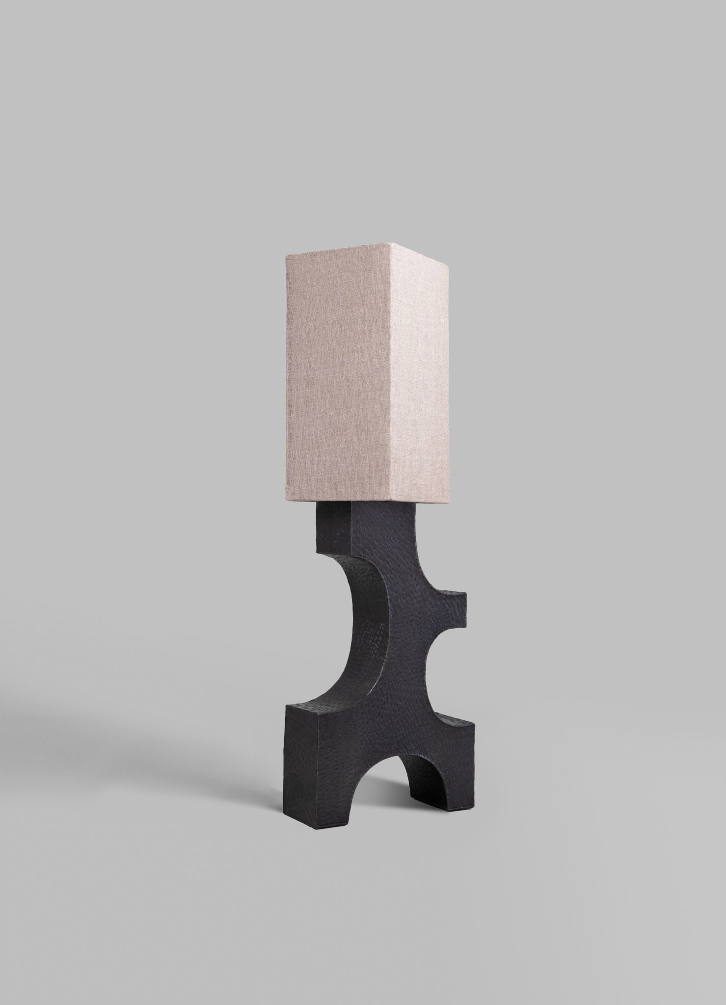 A modern table lamp featuring a black textured wood base with a distinctive curved design and a rectangular beige fabric lampshade.