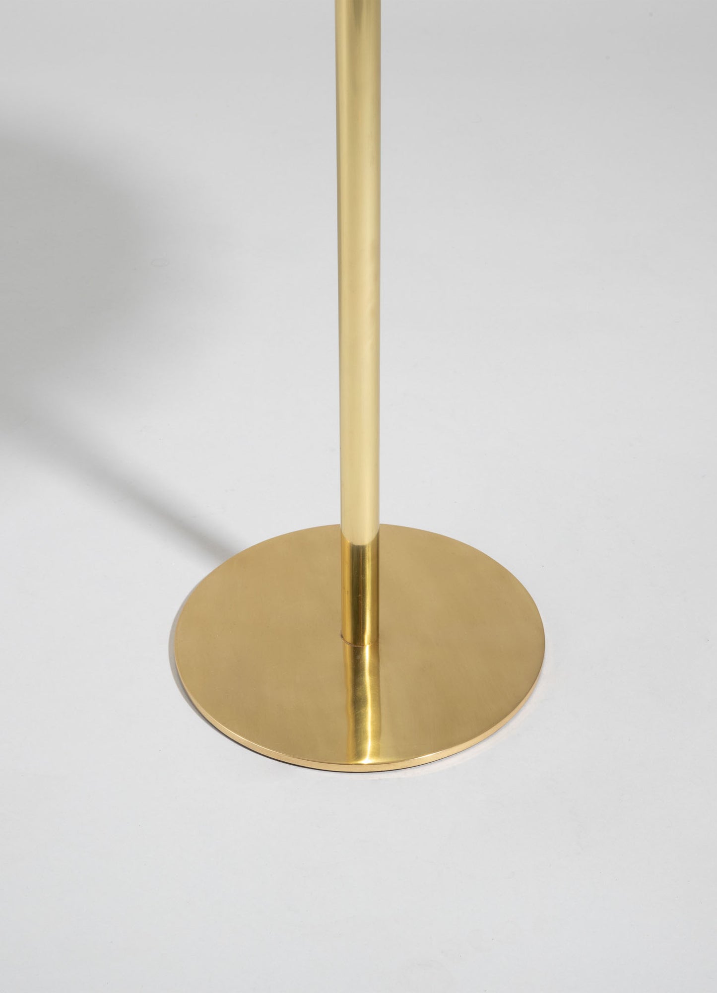 A modern brass floor lamp with a circular base and slim vertical stem, featuring a polished gold finish.