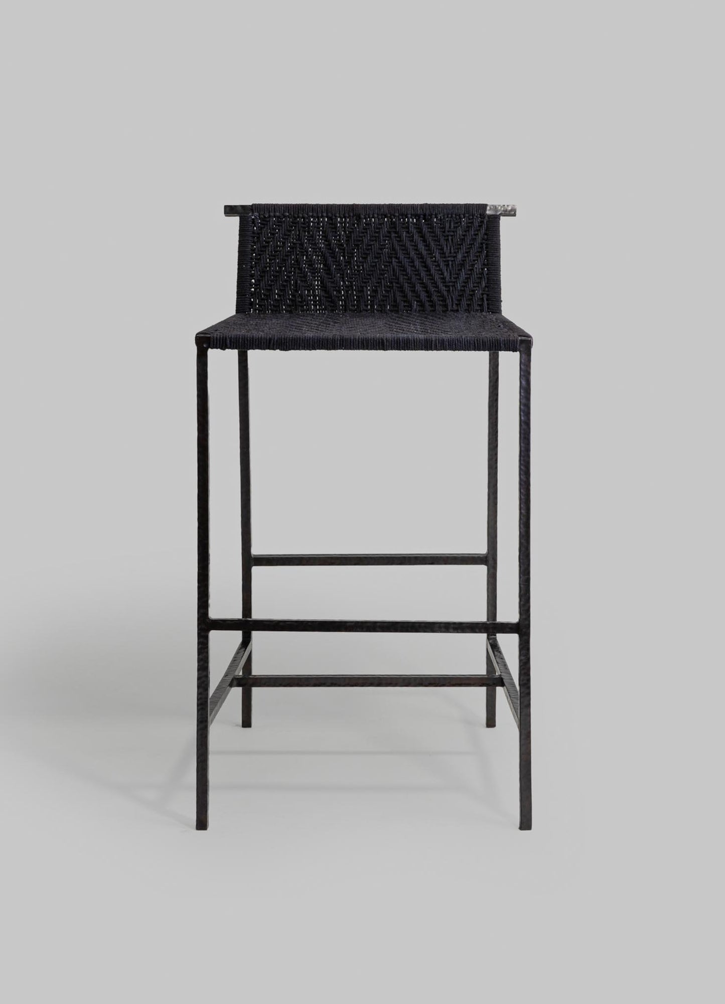 A black woven stool with a textured, patterned fabric seat and a minimalist metal frame with a matte finish, set against a plain light gray background.