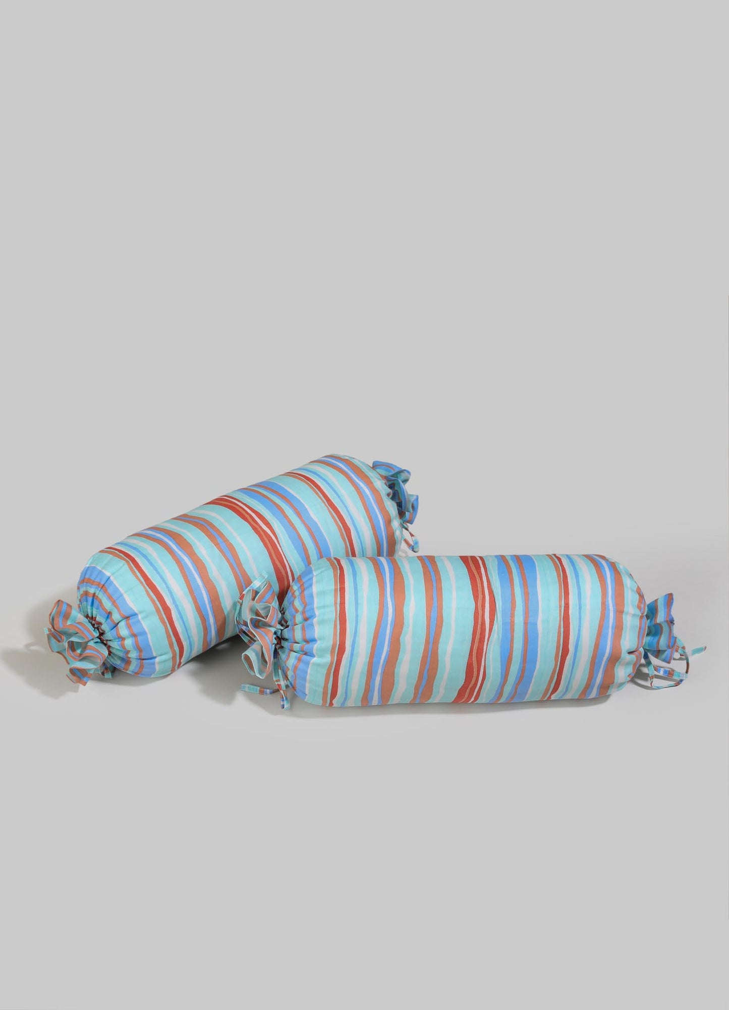 Striped fabric bolster cushions with multicolored horizontal lines in shades of blue, red, and beige, featuring ruffled ends tied with matching fabric bows.