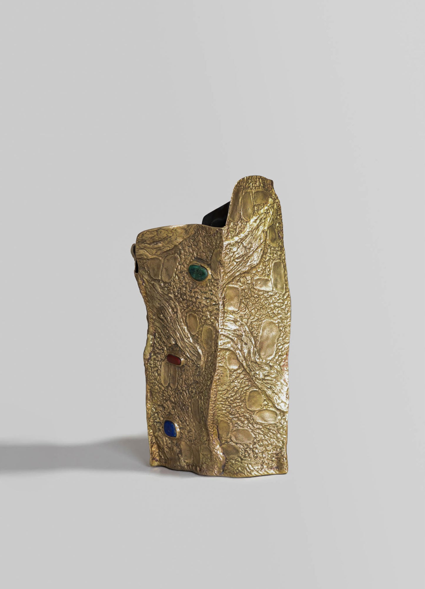 A gold-toned resin sculpture resembling a lizard with a textured surface and embedded colored stones, featuring a sculptural, handcrafted style on a plain background.