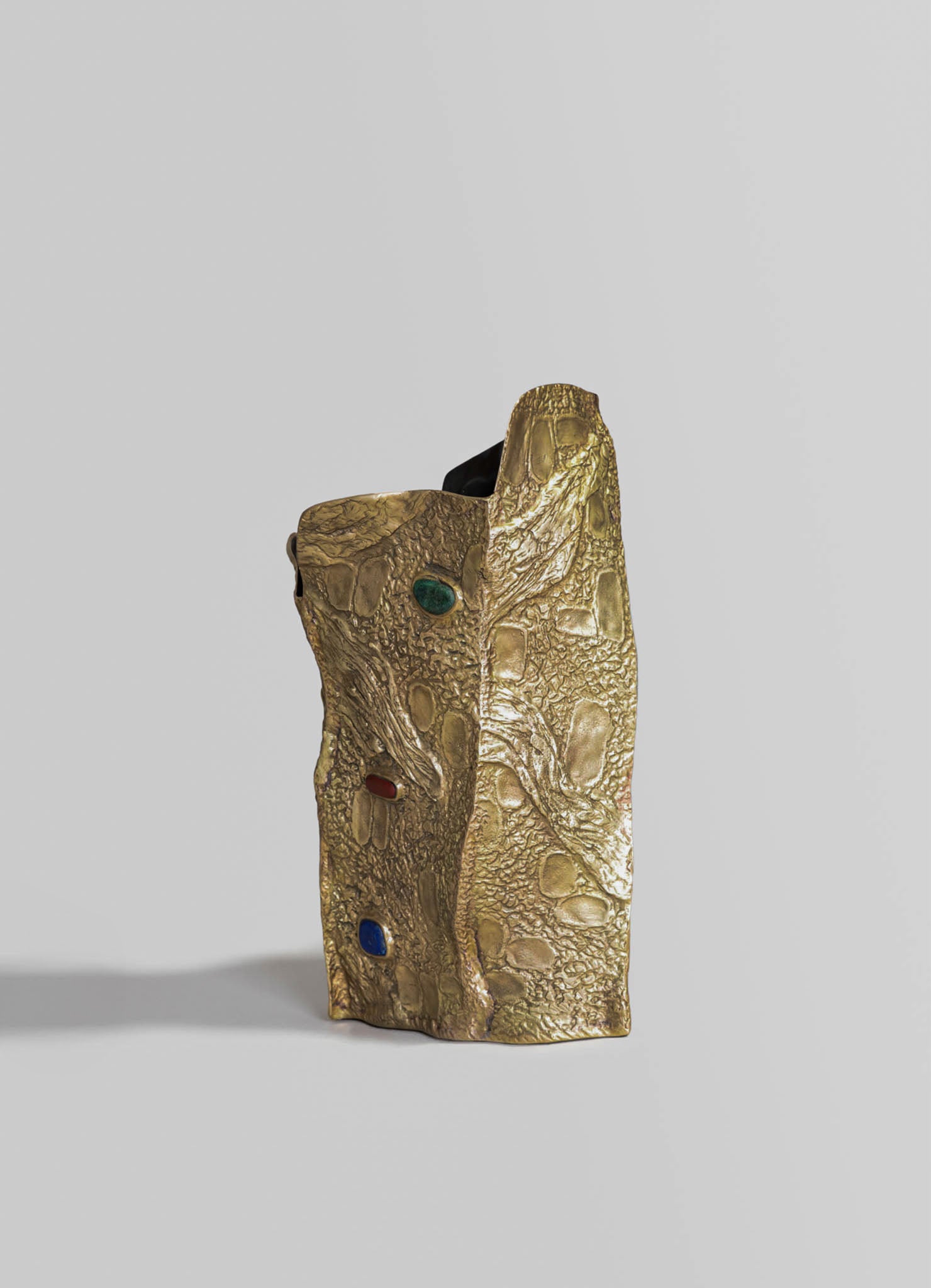 A gold-toned resin sculpture resembling a lizard with a textured surface and embedded colored stones, featuring a sculptural, handcrafted style on a plain background.