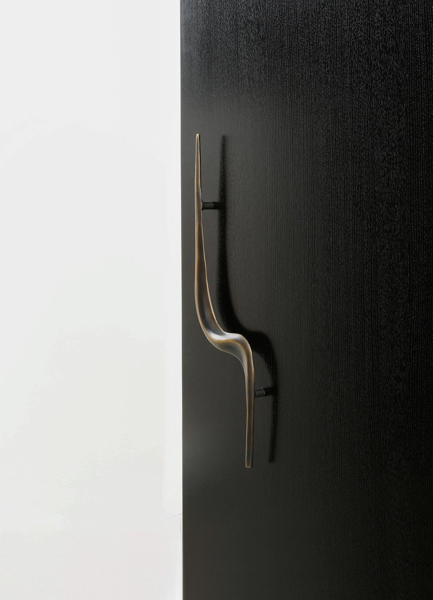 A modern black door handle with a sleek, curved design and a metallic finish, mounted on a textured black door. The handle has a minimalist appearance and is set against a plain background.