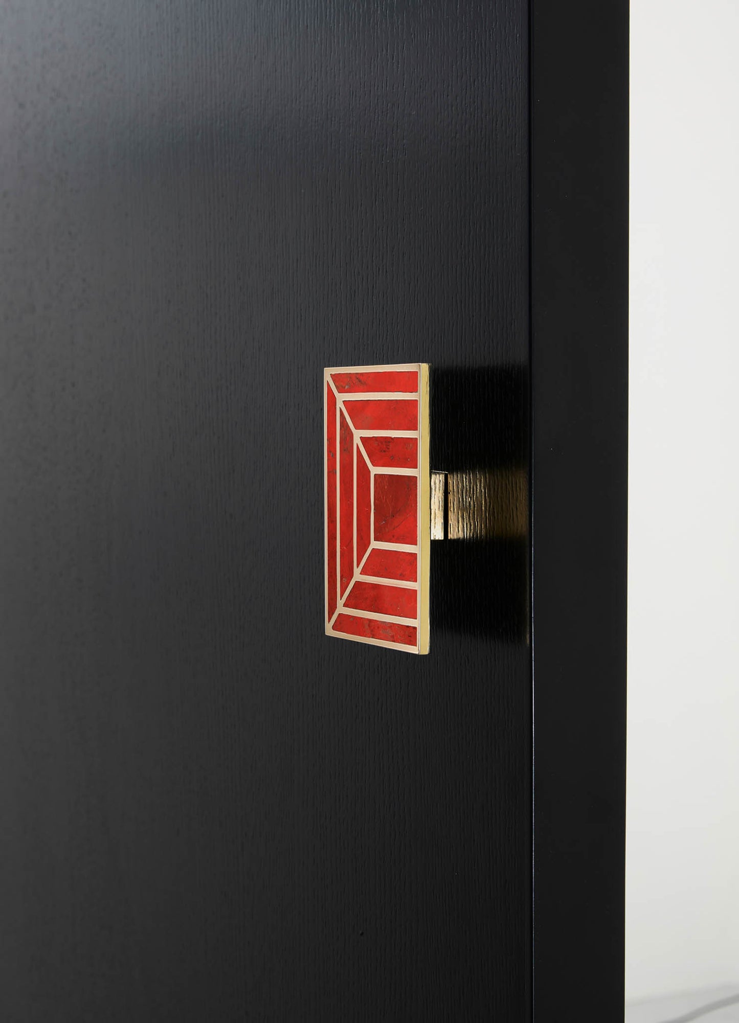 A black wooden panel with a textured matte finish, featuring a decorative rectangular metal handle with a red and gold geometric pattern. The design has a contemporary and minimalist style.
