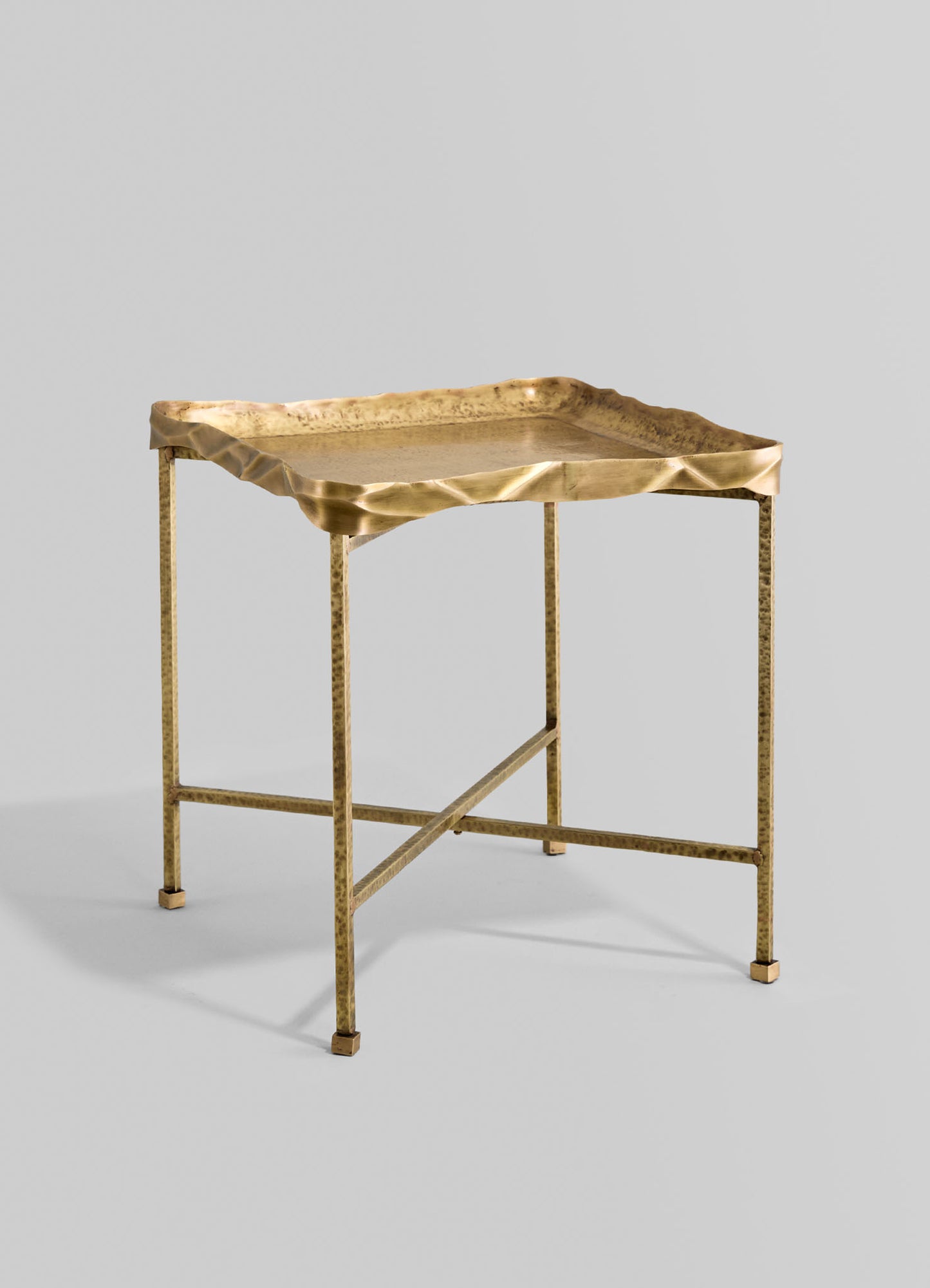 A metal side table with a hammered brass finish, featuring a square top with uneven, sculptural edges and slender, straight legs.