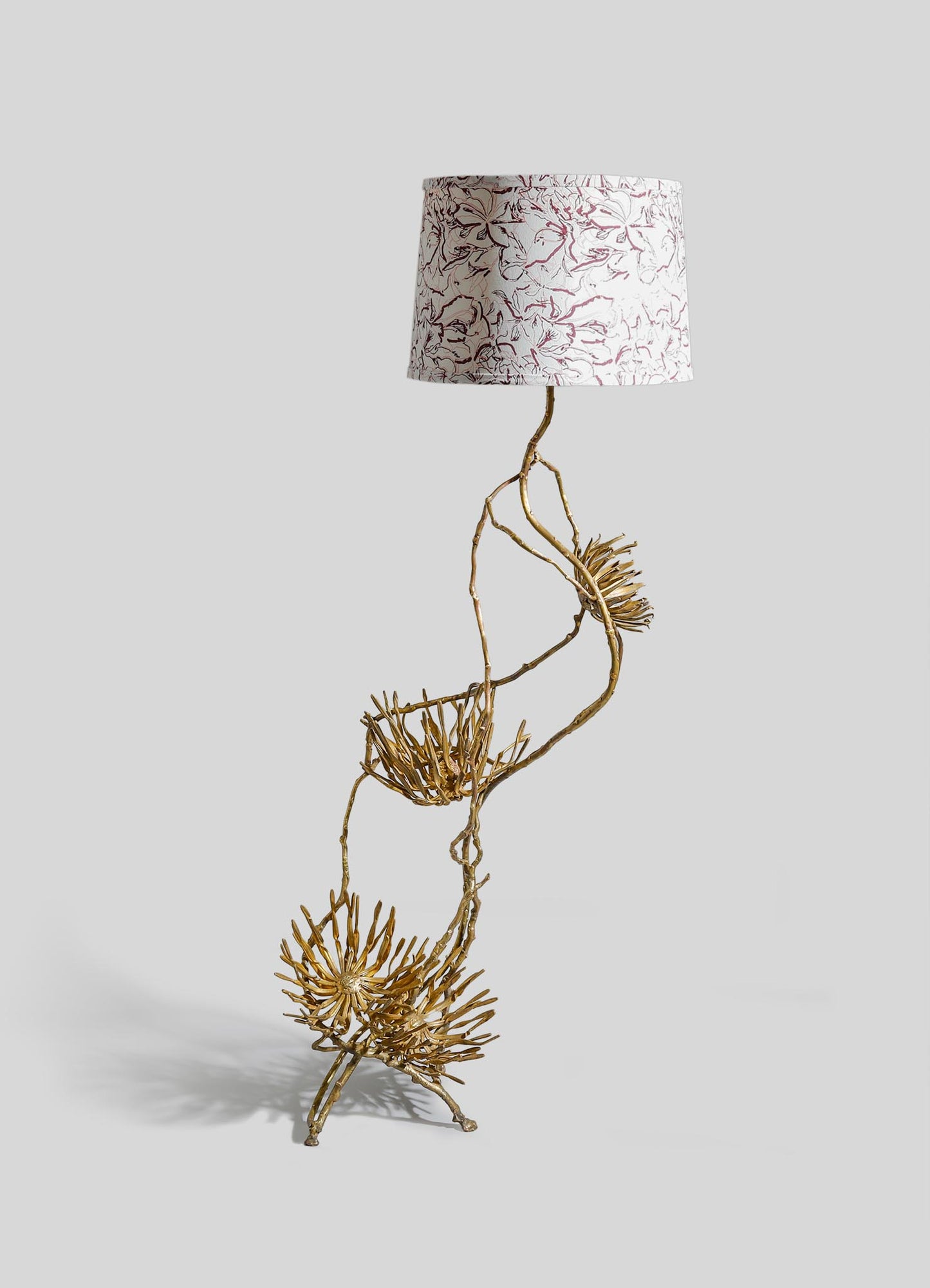 A table lamp with a base made of sculptural, natural-looking branches and a brass finish, topped with a cylindrical fabric lampshade featuring a red and white floral pattern.