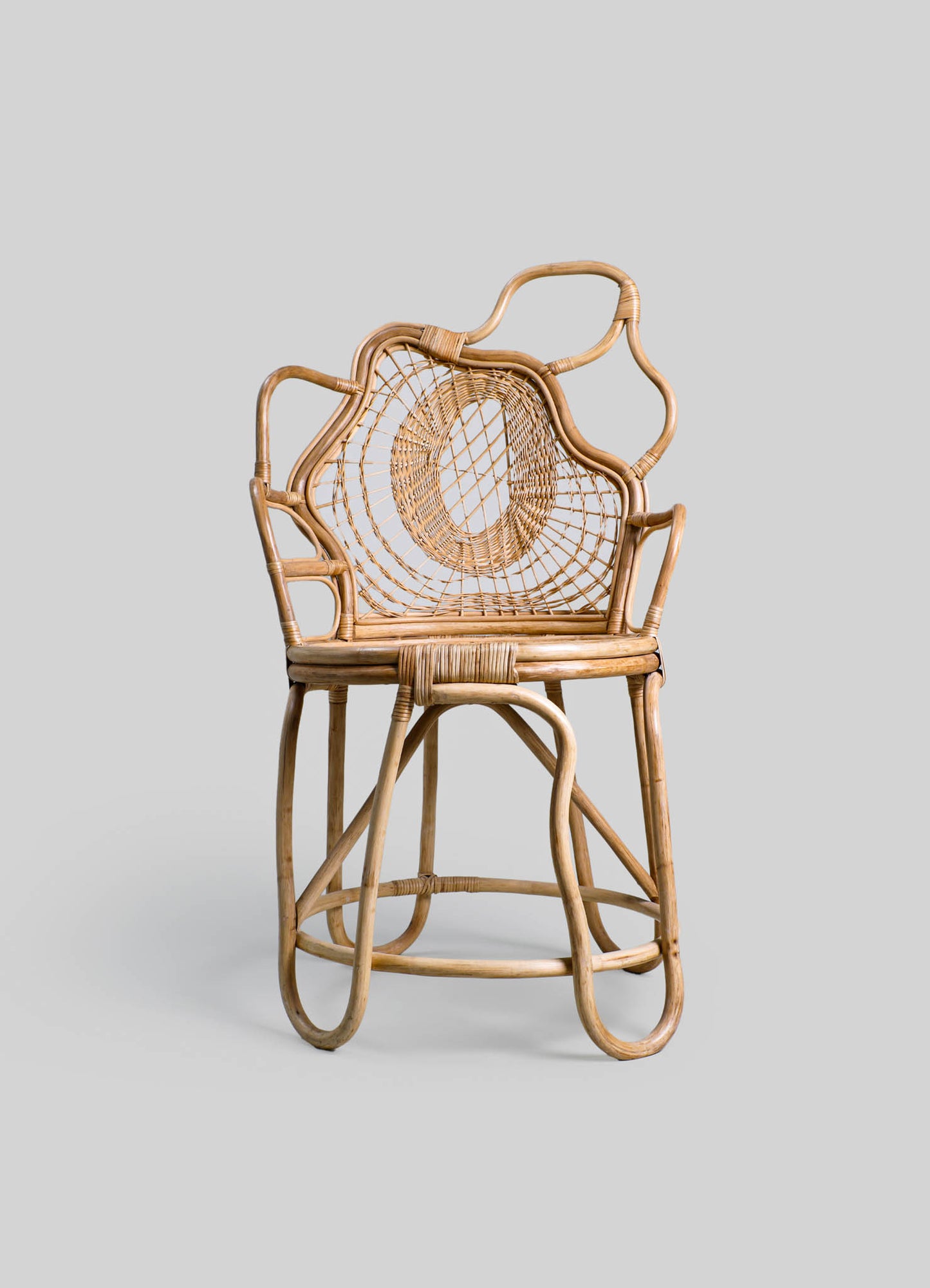 Rattan armchair with a woven cane backrest and seat, featuring a sculptural, organic shape with curved armrests and a high back. The natural wood finish emphasizes a handcrafted, rustic style.