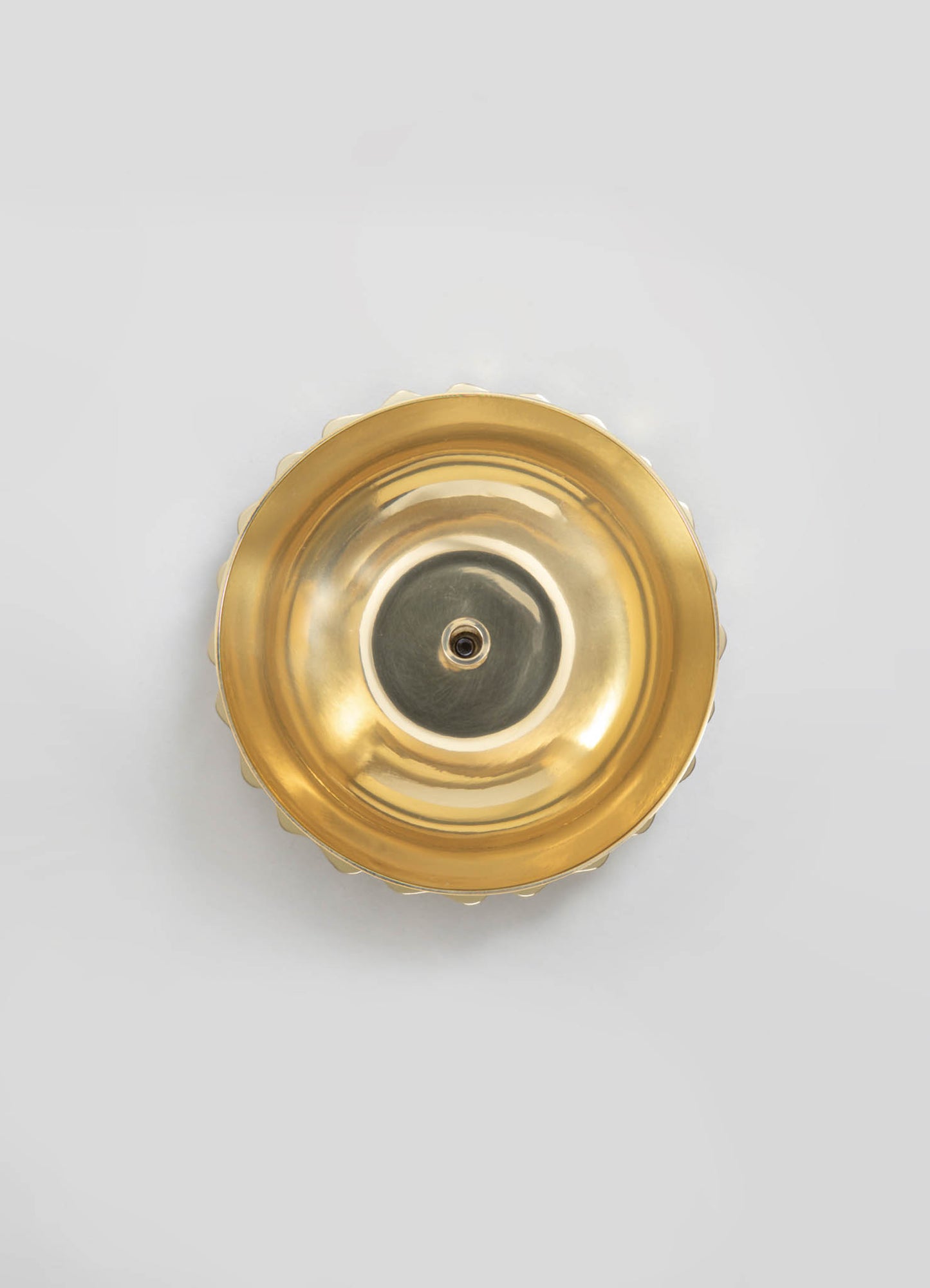 A round brass candle holder with a polished, reflective surface and scalloped edges. The design is sleek and contemporary, emphasizing metallic gold tones and simple geometric form.