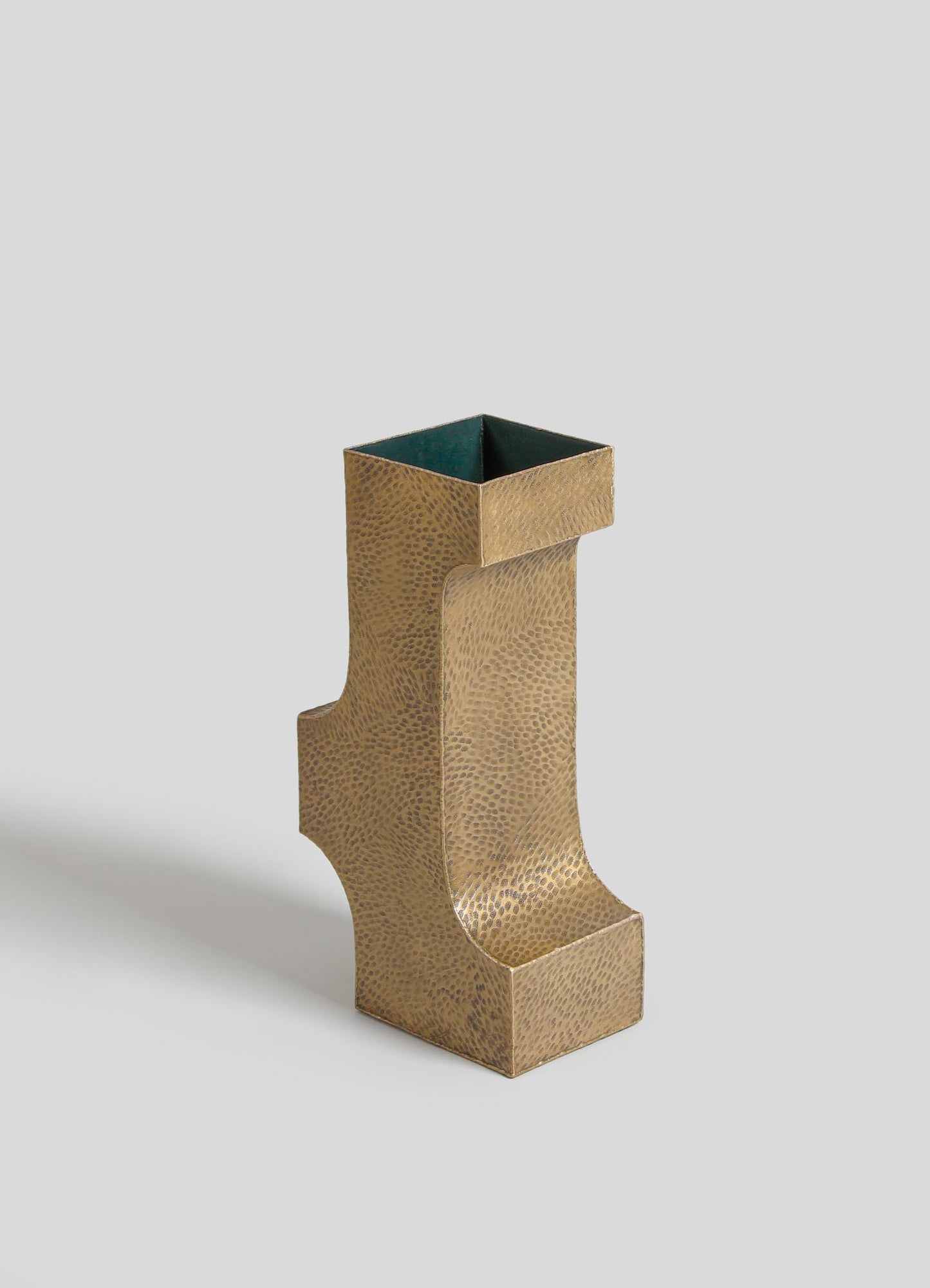 A gold-toned metal vase with a textured, hammered finish and a modern, sculptural shape featuring angular lines and a high-gloss interior.