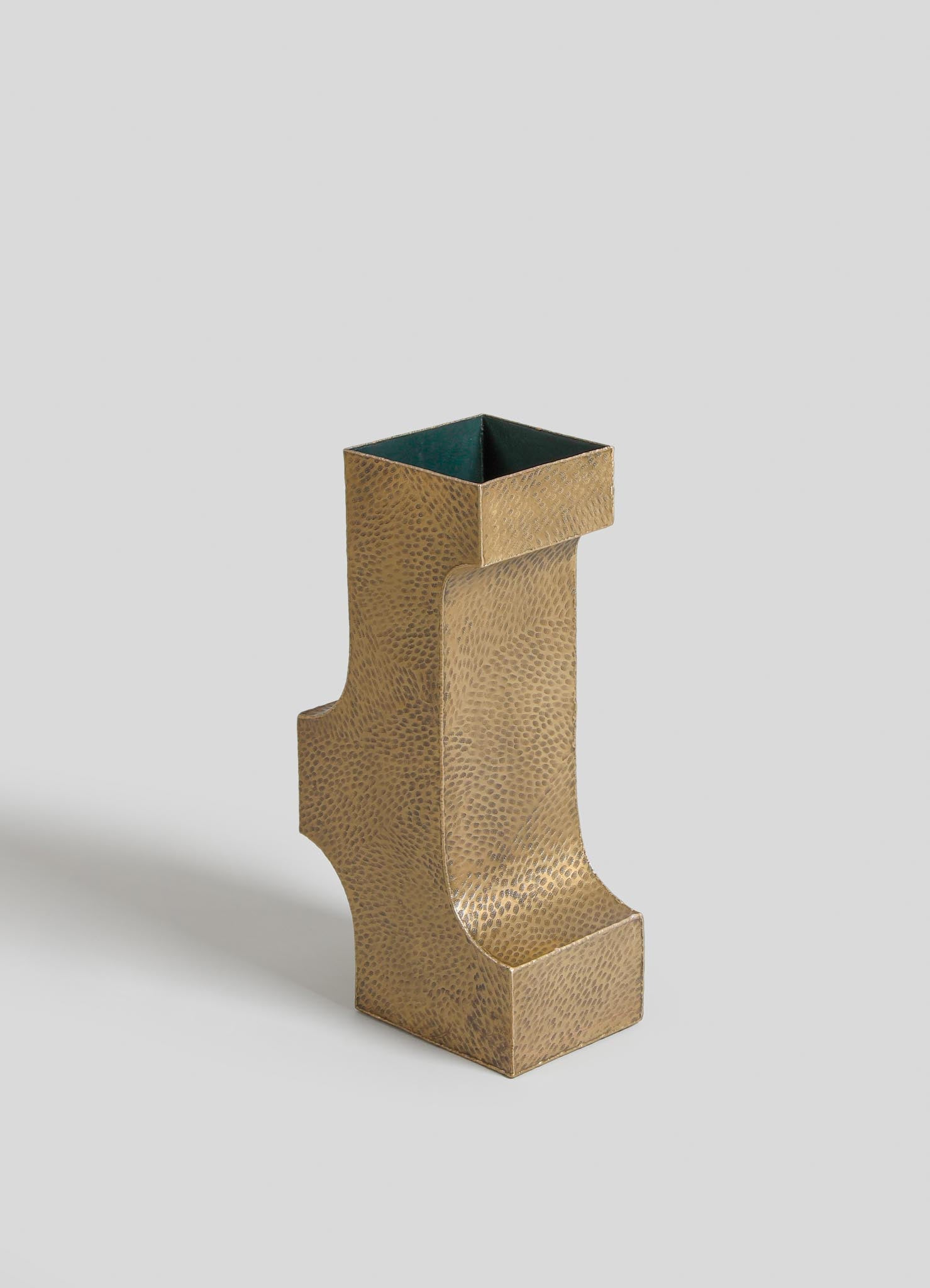 A gold-toned metal vase with a textured, hammered finish and a modern, sculptural shape featuring angular lines and a high-gloss interior.