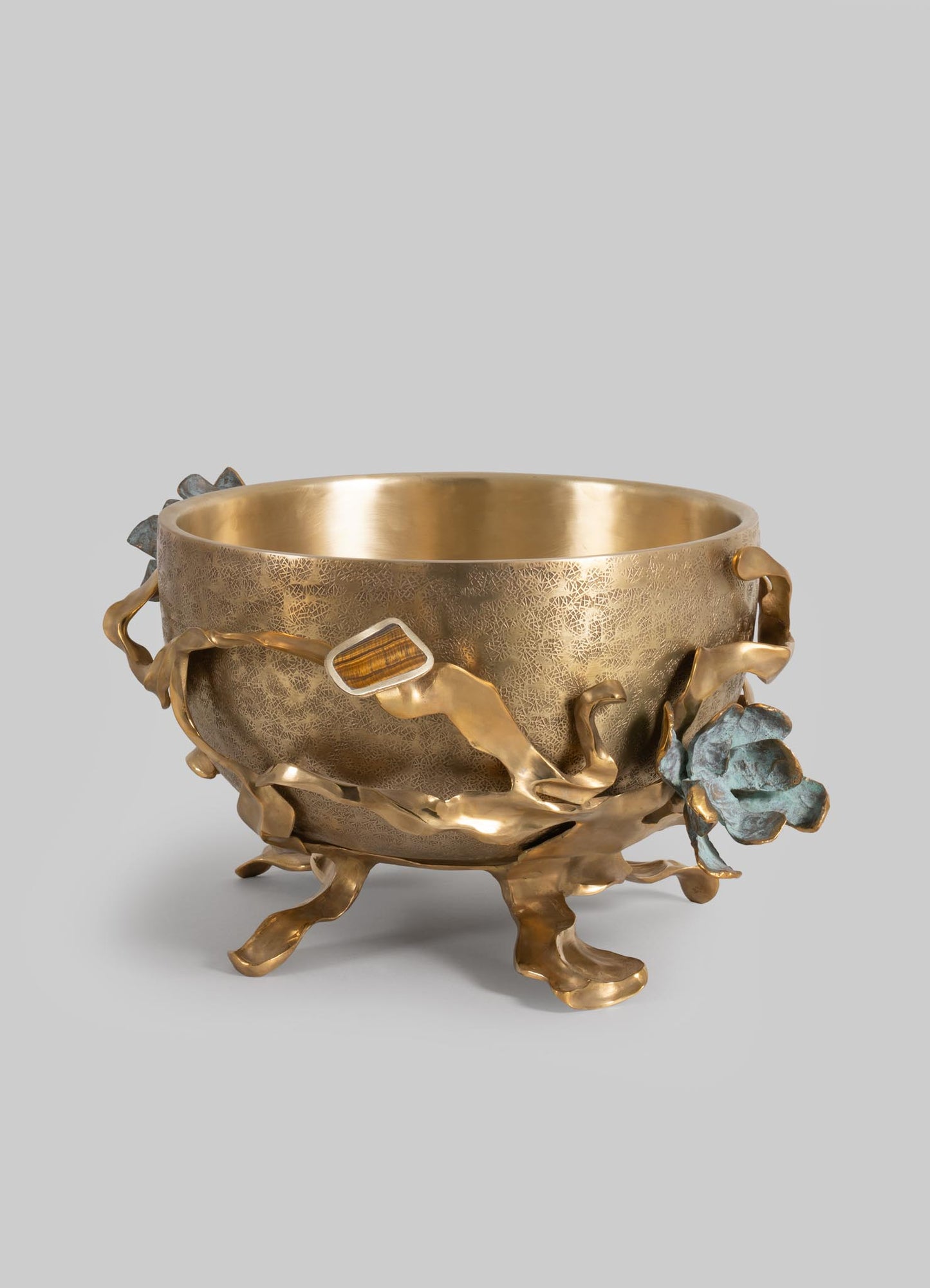 A decorative metal bowl with an intricate textured surface and organic, flowing floral and leaf motifs in brass and patinated finishes, on a plain background.