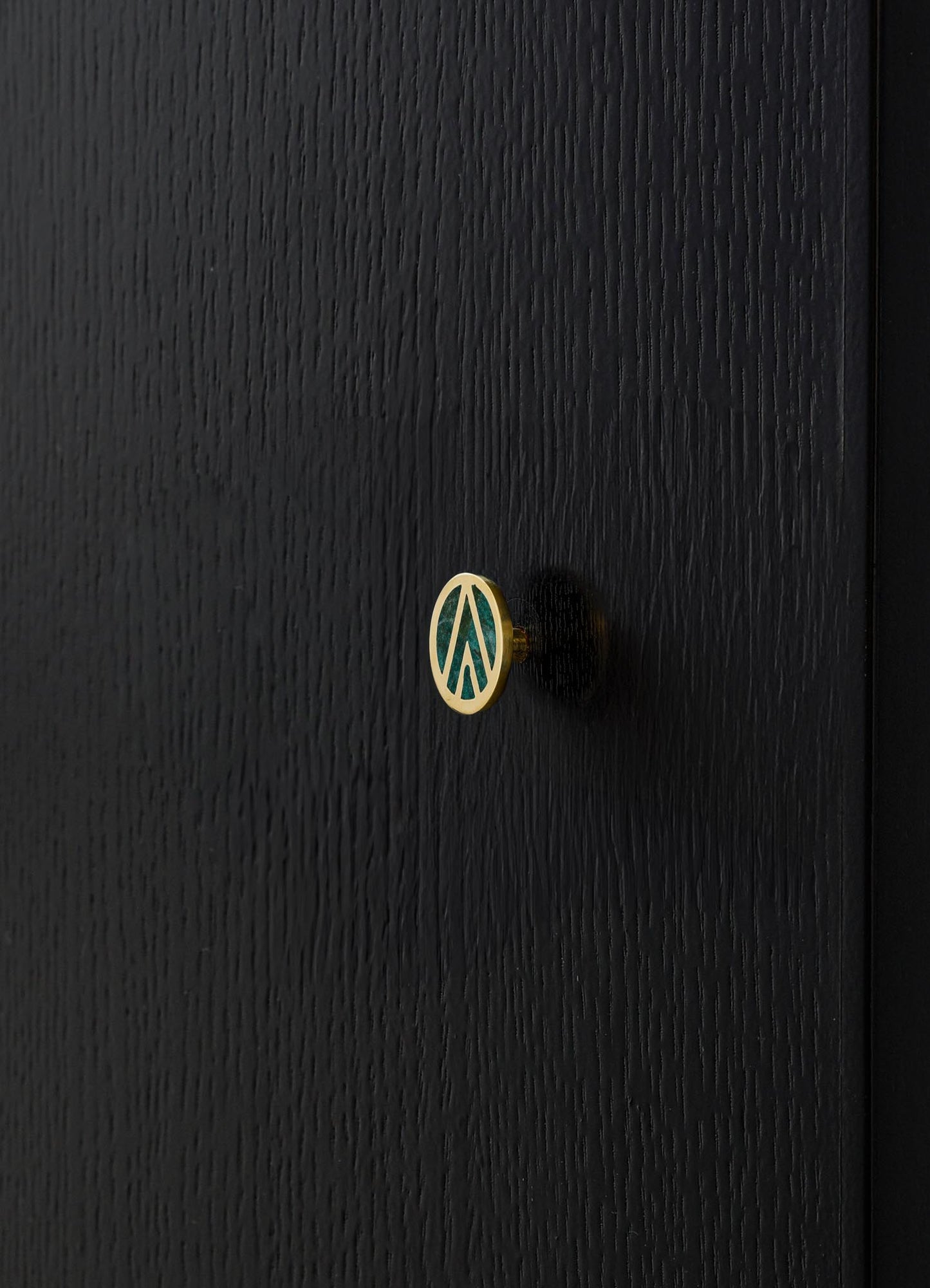A black wooden surface with a small circular decorative knob featuring a gold rim and a teal geometric pattern. The surface has a textured wood grain finish.