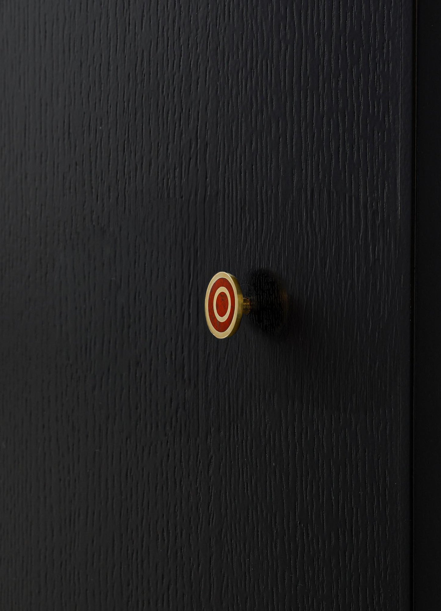 A black wooden surface with a textured finish features a small, round decorative knob with red and white concentric circles, casting a shadow on the wood.