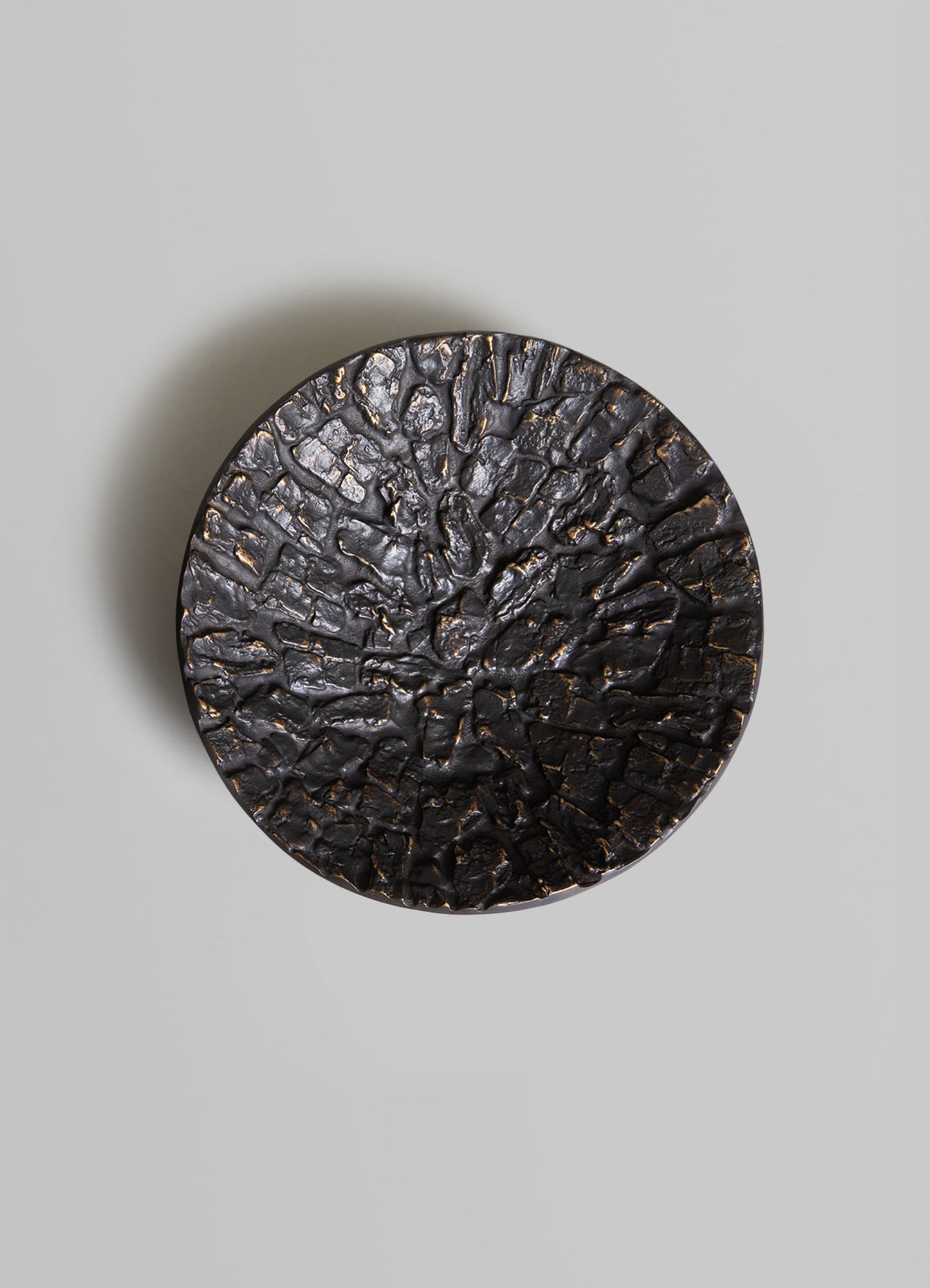 A round decorative tray with a textured, cracked surface in dark, metallic tones and subtle gold accents.