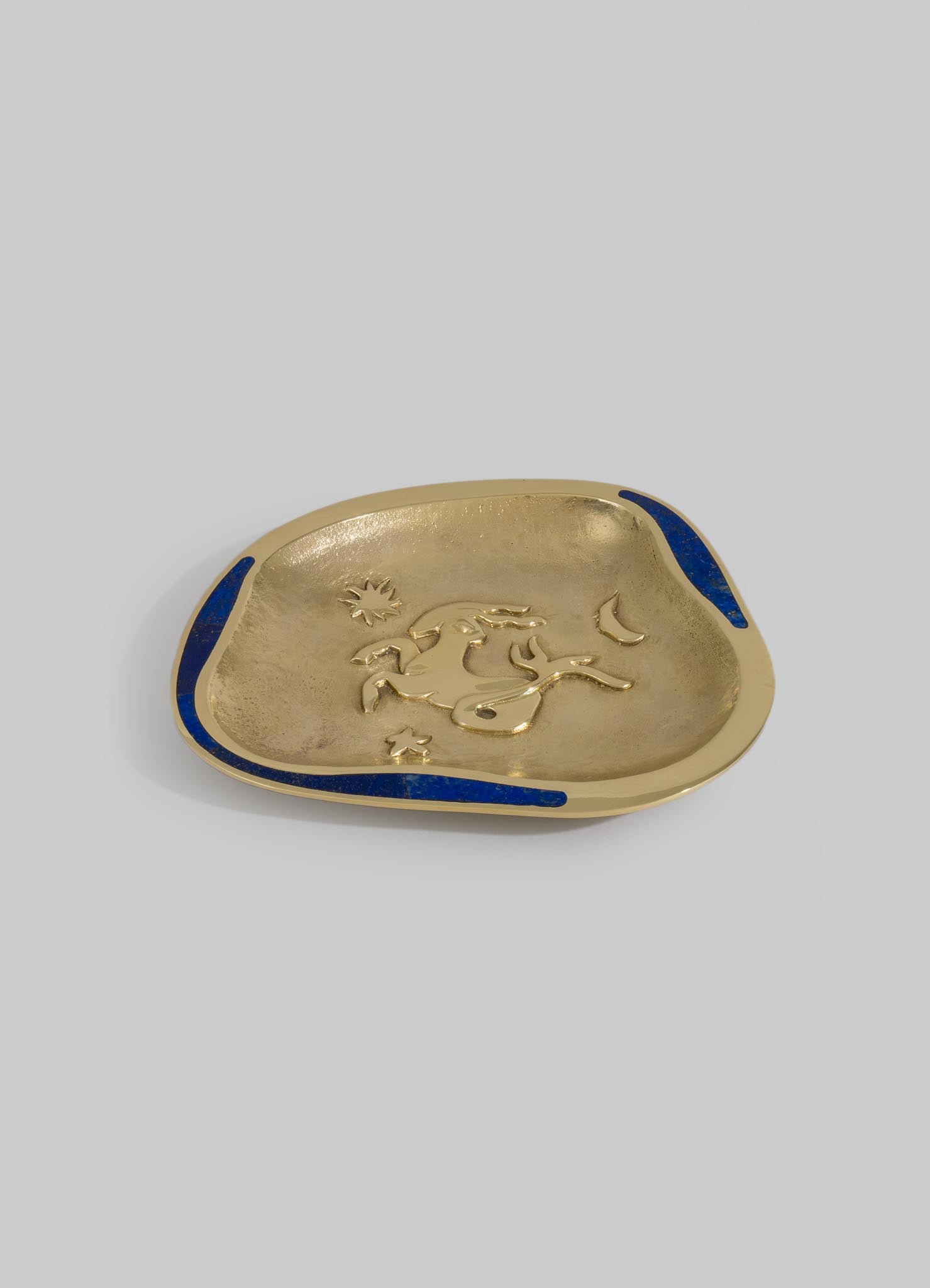 A decorative gold-colored dish with a raised animal motif in the center, accented with blue enamel border details, made of metal.
