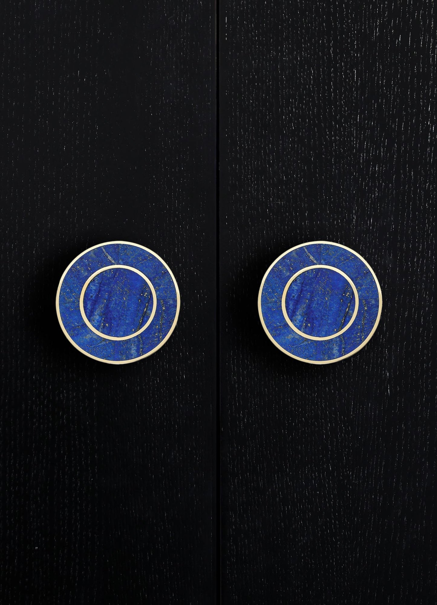 Round ceramic drawer pulls with a vivid blue glaze and gold speckled pattern, framed by white borders, mounted on a black textured surface.